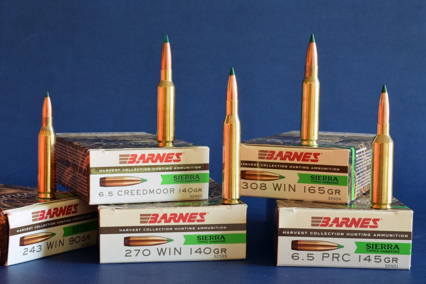 A close-up view of several boxes and individual cartridges from the Barnes Harvest Collection, loaded with Sierra Tipped GameKing bullets. Each cartridge is neatly positioned to display the brass casing, polymer-tipped projectile, and clean manufacturing finish. Visible calibers include options for .223 Remington, .243 Winchester, 6.5 Creedmoor, and .308 Winchester, among others. The arrangement is on a neutral background, highlighting the shiny brass and distinctive bullet tips. The image emphasizes the variety of loads offered in this line. It reflects the brand’s focus on deer-hunting performance and quality ammunition construction.