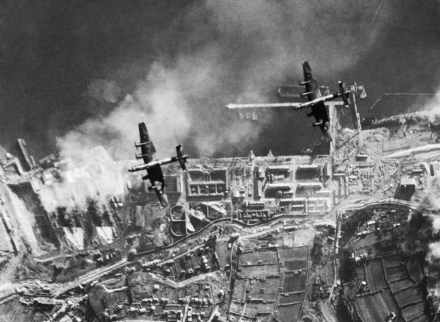 A formation of Handley Page Halifax heavy bombers attacking German Navy ships at Brest, France, during World War II. The bombers are shown overhead as they release their payloads against warships and facilities in the port. Brest was a major base for German battleships, cruisers, and U-boats, making it a high-priority target for the RAF. The Halifax aircraft fly in tight formation, demonstrating the scale of the operation. Explosions and smoke are visible around the harbor as bombs impact near the ships. These missions were heavily defended by anti-aircraft fire, making them extremely dangerous for bomber crews. The image captures the Halifax in action against Germany’s naval threat in occupied France.