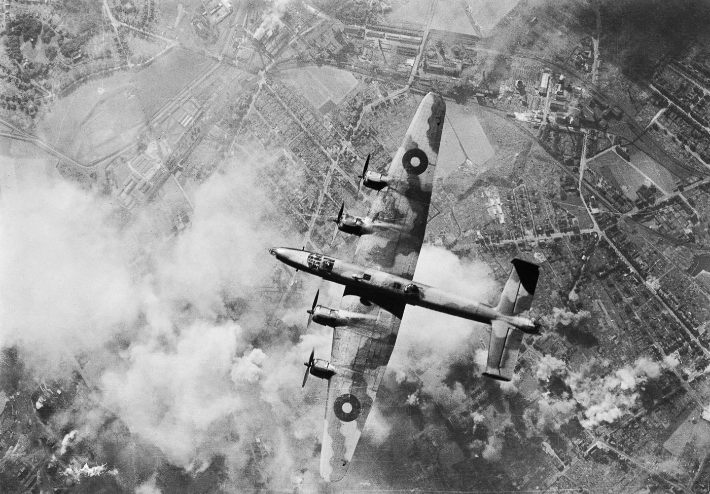 A Handley Page Halifax heavy bomber flying over Wanne-Eickel, Germany, during a World War II bombing mission. The four-engine aircraft is captured mid-flight, part of the Royal Air Force’s nighttime campaign against industrial and strategic targets. Below, the town and its rail yards were frequent objectives due to their importance in German war production. The Halifax is seen from a vantage point that emphasizes its wingspan and bomb-carrying capacity. Missions like this were central to the RAF’s effort to weaken Germany’s ability to sustain the war. The aircraft’s black-painted underside helped conceal it from searchlights and anti-aircraft fire. This image demonstrates the Halifax in active combat operations.