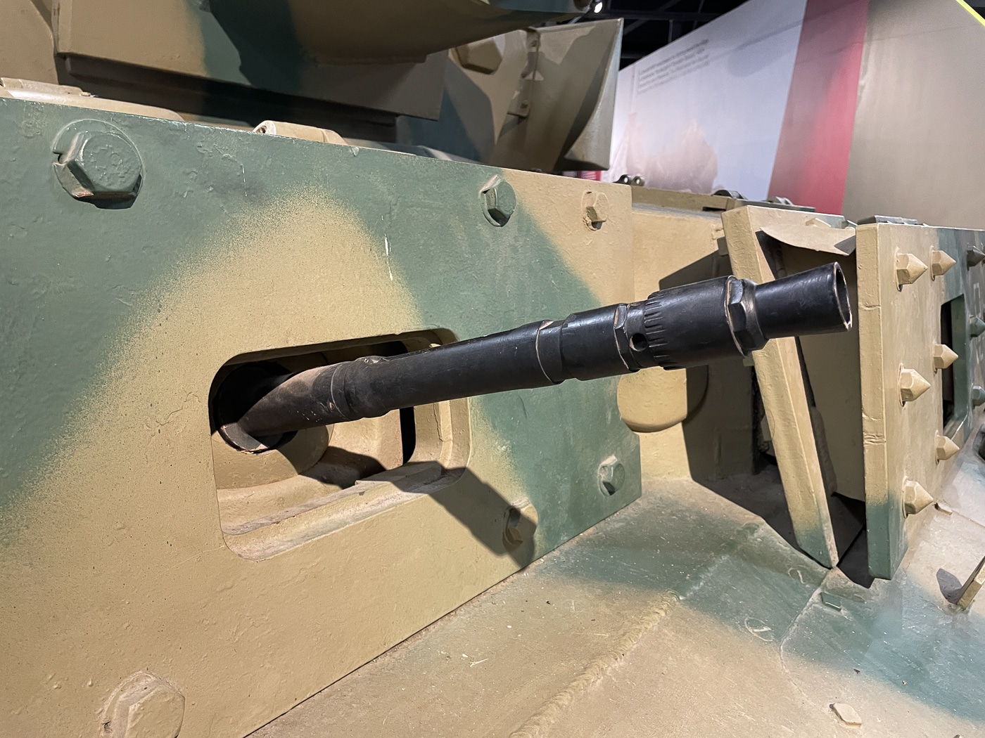 The image shows a close-up of the MG 34 machine gun as mounted on a German Panzer IV tank during World War II. The shot captures the weapon’s perforated barrel cooling jacket, receiver assembly, and ammunition feed port. This MG 34 is configured for armored vehicle use, lacking the bipod found on infantry versions and instead secured within a ball mount. The coaxial or hull-mounted position allowed the gun to be aimed using the tank’s sights. Its dark blued steel finish shows wear from operational use. The background includes sections of the tank’s armor plate, painted in wartime camouflage colors.