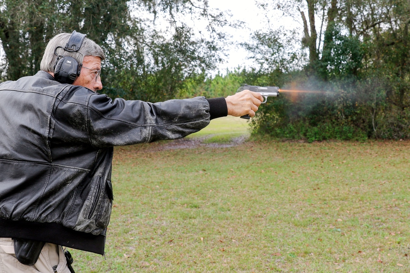 This image shows Massad Ayoob firing the Springfield Armory EMP Ronin pistol one-handed at an outdoor range. He is extending his arm fully, holding the compact 1911-style handgun chambered in 9mm. The EMP Ronin is designed as a smaller, lightweight version of the classic 1911, intended for concealed carry and everyday use. The pistol’s slim grip, shorter barrel, and reduced recoil make it easier to control than a full-size .45 ACP model. Ayoob is demonstrating accuracy and technique with one-handed shooting, which is an important defensive skill. The background shows a typical shooting range environment, with a safe stance and focused expression. The photo emphasizes both the shooter’s expertise and the pistol’s adaptability.