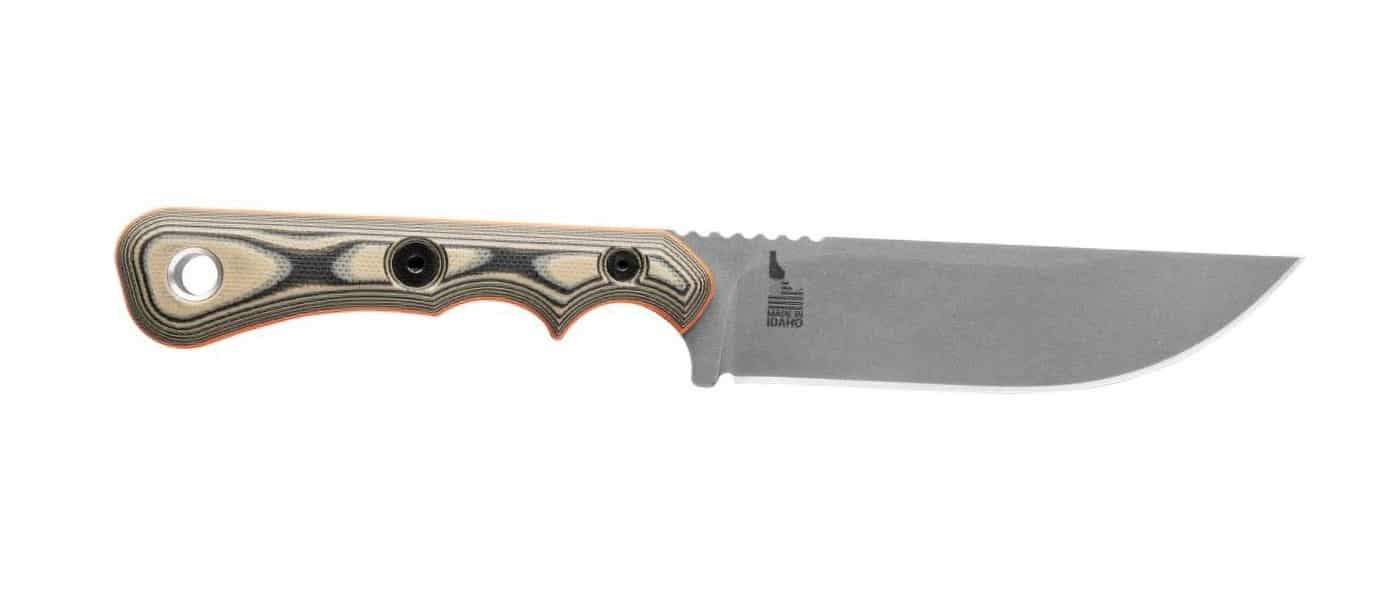 This image focuses on the right side of the TOPS Muley Skinner knife, showing the full length of the 4.5-inch curved blade and the spine’s straight profile. The knife’s black and tan G10 handle scales, secured by four Torx screws, are visible along with the orange G10 liner sandwiched between the scales and the steel tang. The blade’s finish and grind style can be seen, indicating durability and edge retention, as discussed in this TOPS Muley Skinner knife review. The undercut finger grooves and lanyard ring at the rear of the handle show the ergonomic attention to detail. The overall shot demonstrates the knife’s balance between size, function, and safety features for hunters or outdoorsmen. The backdrop is plain or out of focus to keep attention on the knife itself. This image is typical for showcasing blade geometry and material quality in a knife review.
