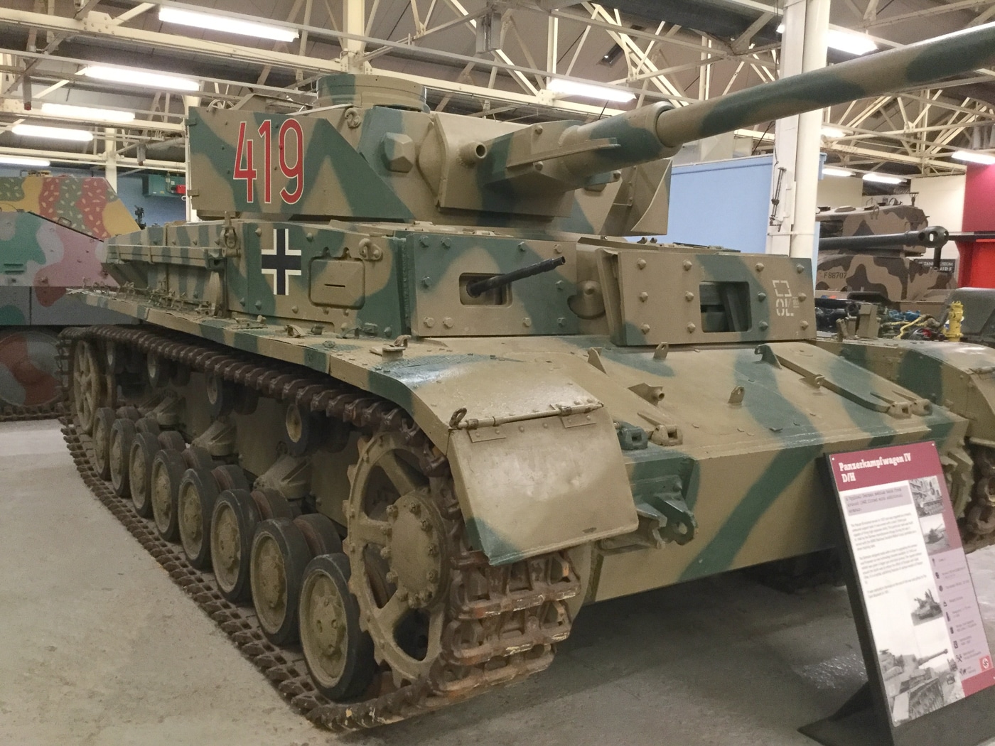 The image shows an early-production German Panzer IV Ausf. H tank with 30mm bolt-on armor plates affixed to the front glacis, similar to the Ausf. G variant. Instead of the later single-piece 80mm armor plate, this transitional model uses visible mounting bolts to secure the additional frontal protection. The tank is painted in a dark wartime camouflage pattern, and the long-barreled 75mm KwK 40 L/48 main gun extends forward with a muzzle brake. Side armor skirts, or Schürzen, are partially visible along the hull. The tank is photographed in an outdoor setting, highlighting the front hull where the armor modification is most apparent. This example reflects the incremental upgrades made during mid-1943 as production transitioned between variants.