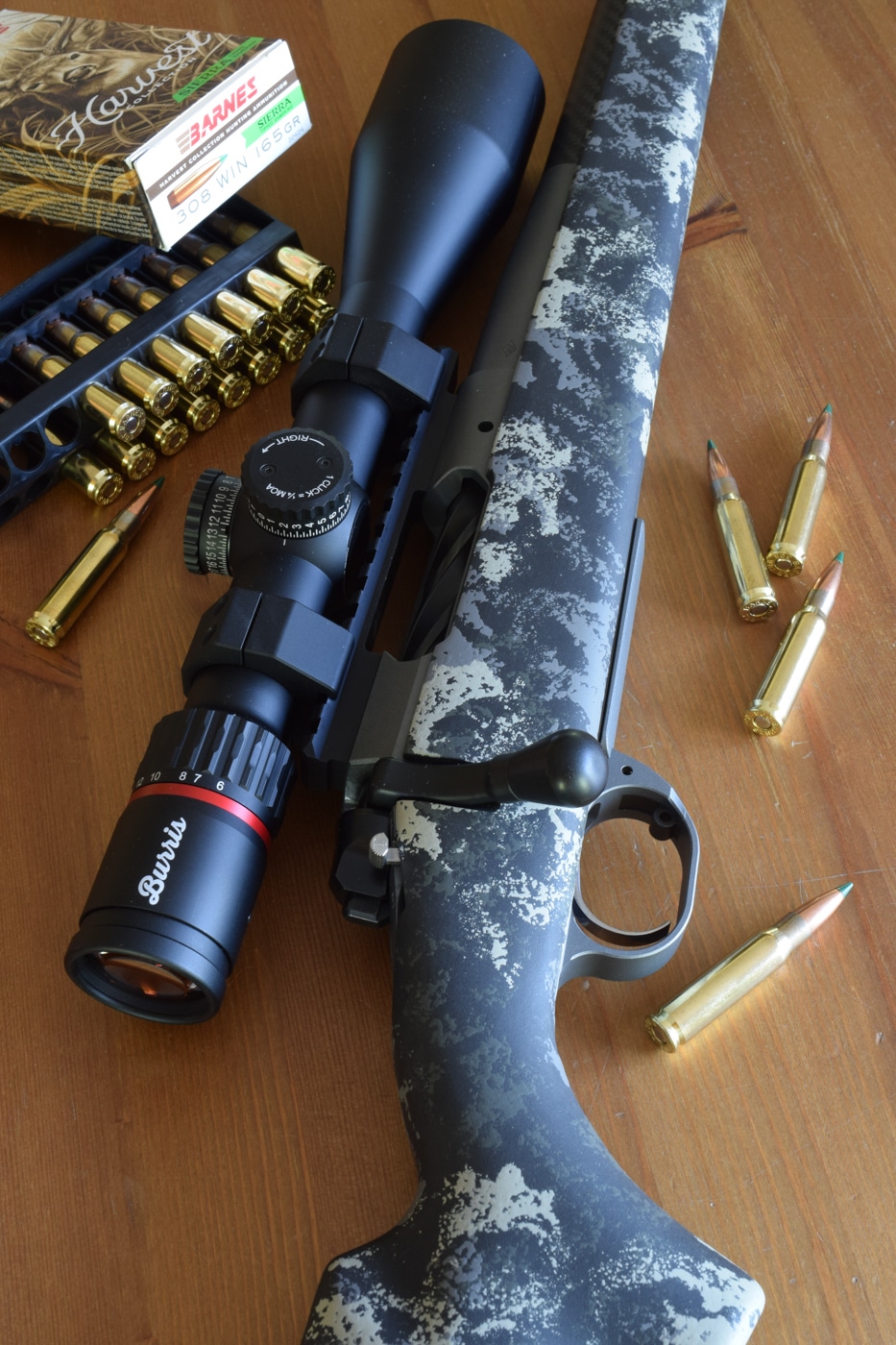 Full side view of a Springfield Armory Boundary bolt-action rifle resting on a shooting bench. The rifle features a short, threaded barrel, textured stock, and mounted riflescope. Chambered in .308 Winchester, this firearm was used in accuracy and velocity testing for Barnes Harvest Collection ammunition loaded with Sierra Tipped GameKing bullets. The scope’s turrets and magnification adjustment ring are clearly visible. Background shows an outdoor range setup with targets in the distance. The image highlights the rifle’s compact, practical hunting design.