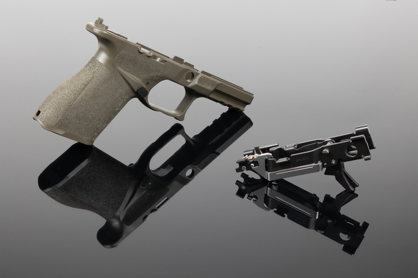 The image displays a Springfield Armory Echelon 4.0C grip module with the Central Operating Group fully installed. The grip module is made from textured black polymer, and the Central Operating Group — visible through the module’s openings — houses the trigger assembly and other key fire control components. This setup demonstrates how the serialized receiver (Central Operating Group) is completely separate from the grip frame, making the firearm modular and highly customizable. The installed module includes a magazine release and cutouts for the slide stop lever, all visible in the image. The photograph is well-lit, highlighting the clean fit and alignment between the grip module and the Central Operating Group. The background is plain, making the gun parts the focus of the shot. This picture is ideal for showing how the Echelon 4.0C’s modular construction sets it apart from traditional pistol designs.