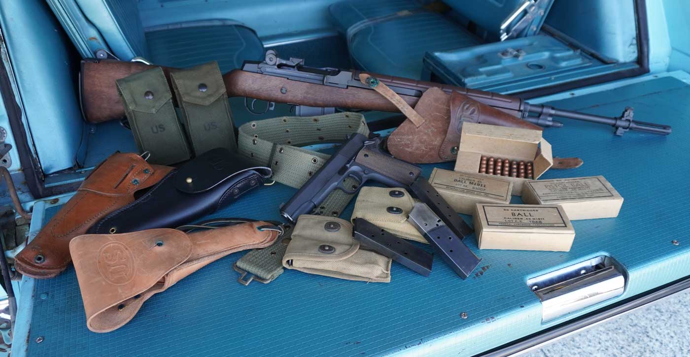 The image presents the Springfield Armory M1A rifle and Mil-Spec 1911 pistol arranged together with a variety of period-correct accessories. Included in the photo are reproduction or original G.I.-style ammunition boxes, both .308 and .45 ACP, as well as matching magazines for each firearm. The 1911 is paired with a classic leather military holster, and nearby are canvas web gear items such as a magazine pouch and a field belt. The overall setup aims to replicate an authentic mid-20th-century U.S. military field kit. The firearms and accessories are clean and organized, giving a clear look at each component. This photo visually demonstrates how modern Springfield models can fit seamlessly with historical surplus gear and collectible accessories, perfect for articles about military-style collections, reenactment setups, or gear recommendations for Springfield owners. The lighting and background are neutral, ensuring that all elements are easy to identify.