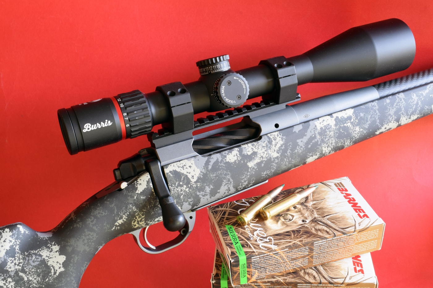 A Springfield Armory Model 2020 Waypoint bolt-action hunting rifle positioned on a shooting bench, equipped with a mounted Burris Fullfield 6-24x50 riflescope. The rifle features a carbon-fiber wrapped barrel, textured stock, and a bipod attachment point. The scope has a large objective lens and precise adjustment turrets. This setup was used in testing Barnes Harvest Collection ammunition loaded with Sierra TGK bullets. Lighting and camera angle highlight the clean lines of the rifle and the scope’s mounted position.