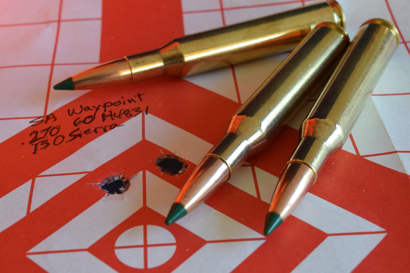 Close-up of TGK bullets seated in brass cases, prepared by the author for handloading accuracy tests. Next to the cartridges is a target with three to five impacts clustered tightly within the bullseye. The polymer-tipped projectiles are arranged to show uniform seating depth and clean case preparation. The image was taken at a shooting bench, with clear focus on both ammunition and results. The performance shown reflects both careful load development and the bullet’s consistent flight characteristics.
