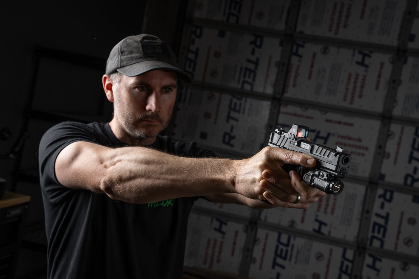 The author is pictured holding the Springfield Armory Echelon 4.0C Comp 9mm pistol. The handgun features a black Melonite-finished slide with an integral single-port compensator positioned just behind the tritium/luminescent front sight. A red dot optic is mounted directly to the slide, co-witnessing with U-Dot rear sights. The compact frame uses the Adaptive Grip Texture for secure handling and includes interchangeable backstraps for fit customization. The author maintains a firm grip, illustrating the pistol’s ergonomic design and balanced proportions. The overall presentation emphasizes the firearm’s suitability for concealed carry, training, and general-purpose use.