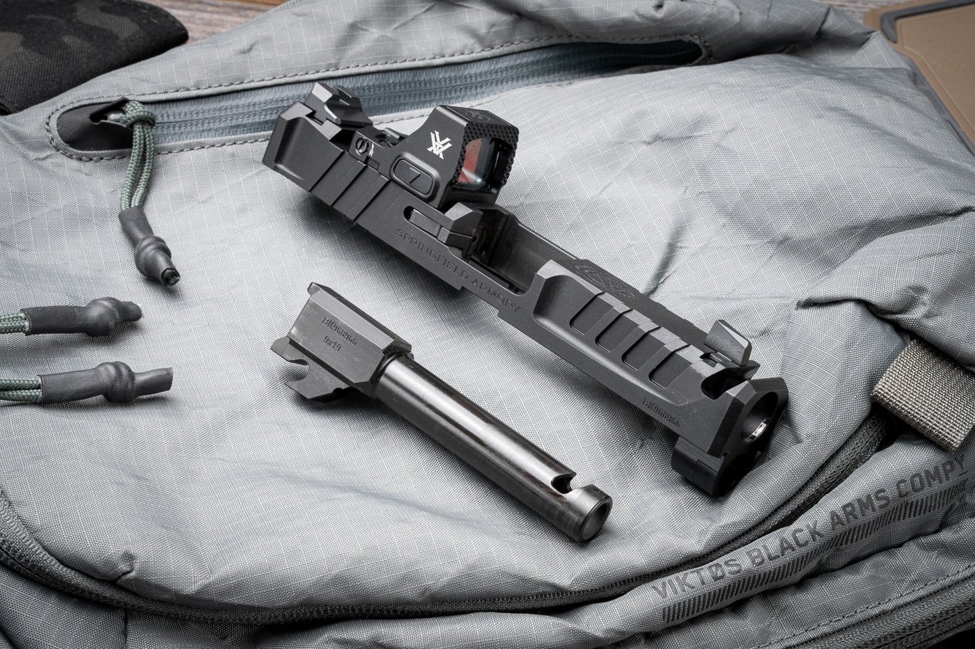 A detailed image of the Springfield Armory Echelon 4.0C Comp’s barrel and slide removed from the pistol frame. Both the 4-inch hammer-forged barrel and the billet-machined slide feature an integral single-port compensator cut, precisely aligned to vent gases upward and reduce muzzle rise. The barrel’s Melonite finish matches the slide’s matte black coating, providing corrosion resistance and durability. Serrations on the slide offer enhanced grip for manipulation, while the compensator port sits just behind where the front sight would be when assembled. This factory-integrated system eliminates the need for threaded barrels or add-on compensators. The photo focuses on the craftsmanship and engineering that contribute to the pistol’s recoil management and reliability.