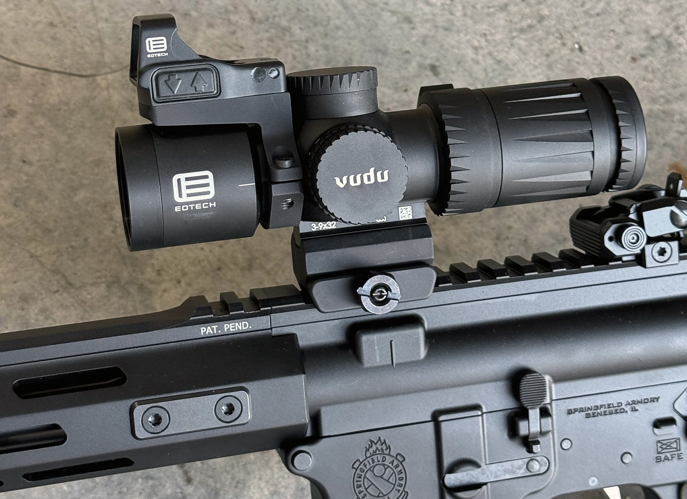 The image is a close-up of the EOTECH Vudu 3-9X32 second focal plane riflescope. The optic is finished in matte black with an anodized surface that reduces glare. Its capped windage and elevation turrets are visible, along with the smooth magnification adjustment ring near the eyepiece. The scope’s compact length and sturdy single-piece body are evident, giving it a solid and rugged appearance. Fine machining lines can be seen in the aluminum housing, and the engraved EOTECH branding is clearly visible on the side. The close-up angle emphasizes the optic’s high-end construction and attention to detail.