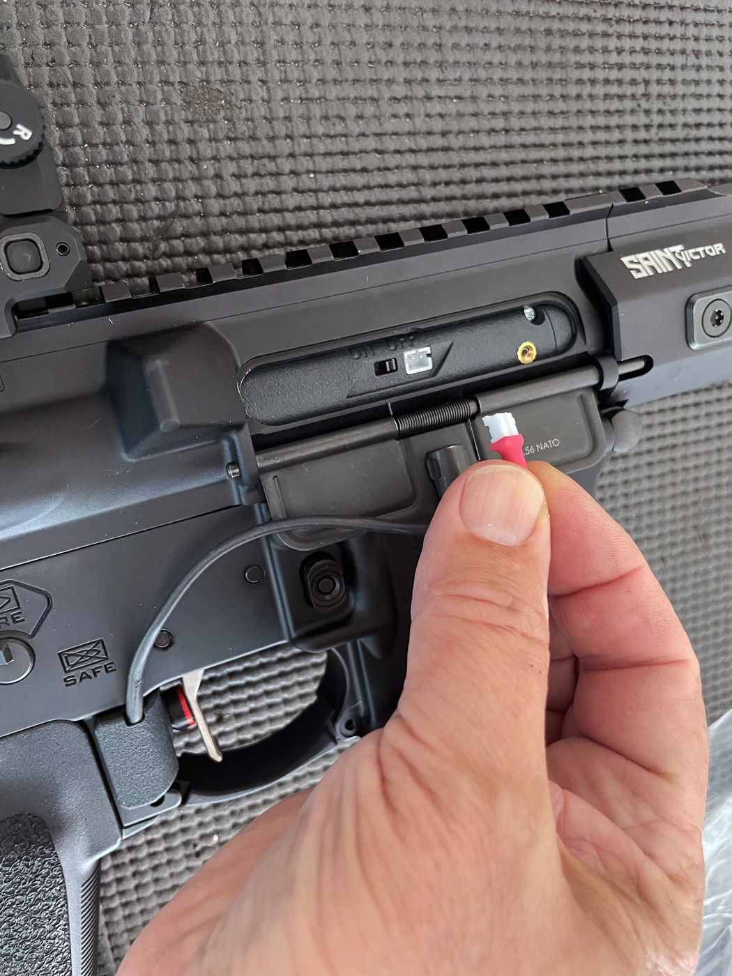Close-up of the thin connection cord running from the trigger activation switch to the Laser Ammo Flash Bolt inside an AR-15 rifle. The cable plugs securely into the Flash Bolt unit, transmitting each trigger press to activate the laser. It is lightweight and flexible to avoid interfering with handling during training. The connection point is located near the rifle’s magwell, keeping it accessible for setup and removal. This cord is essential for linking the mechanical trigger press to the electronic laser system. The image shows the secure fit and streamlined design for unobtrusive operation.