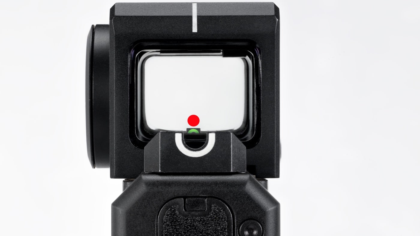 Photo shows a close-up view through the Burris FastFire E red dot sight mounted on a handgun, likely a Springfield Echelon. The red dot is visible in the sight window, perfectly aligned above the front iron sight post, demonstrating co-witness capability. The rear and front iron sights are sharply in focus, confirming that both sighting systems are usable together. The optic’s enclosure and lens are visible around the sight picture, with no obstructions or visual interference. This setup illustrates the benefit of co-witnessing in a duty optic, allowing immediate backup to iron sights if needed. Lighting is balanced to show both the illuminated dot and the physical sights. This photo would help readers of a Burris FastFire E review understand the optic’s compatibility with factory sights.