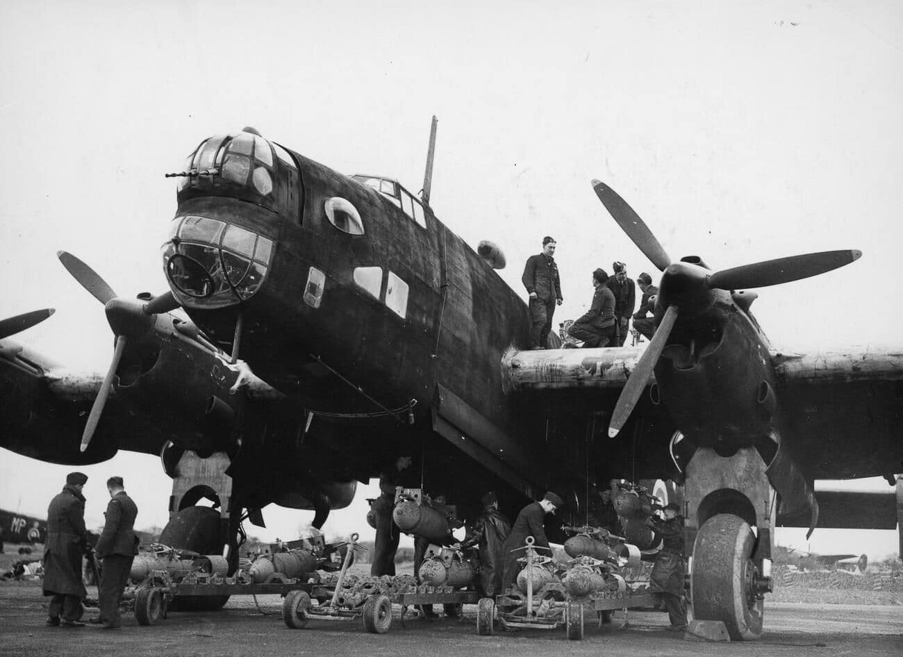 Ground crew loading bombs into the bomb bay of a Handley Page Halifax Mk II during World War II. Several men work beneath the large four-engine bomber, preparing it for a mission. The size of the bomb bay and racks is visible, demonstrating the Halifax’s ability to carry a heavy bomb load of up to 13,000 pounds. The Mk II was one of the early variants of the Halifax and was frequently used in night raids against Germany. Scenes like this were repeated daily across RAF airfields as aircraft were prepared for sorties. The image illustrates the essential role of support crews in maintaining the bombing campaign. Without such preparation, the Halifax could not have carried out its operational role.