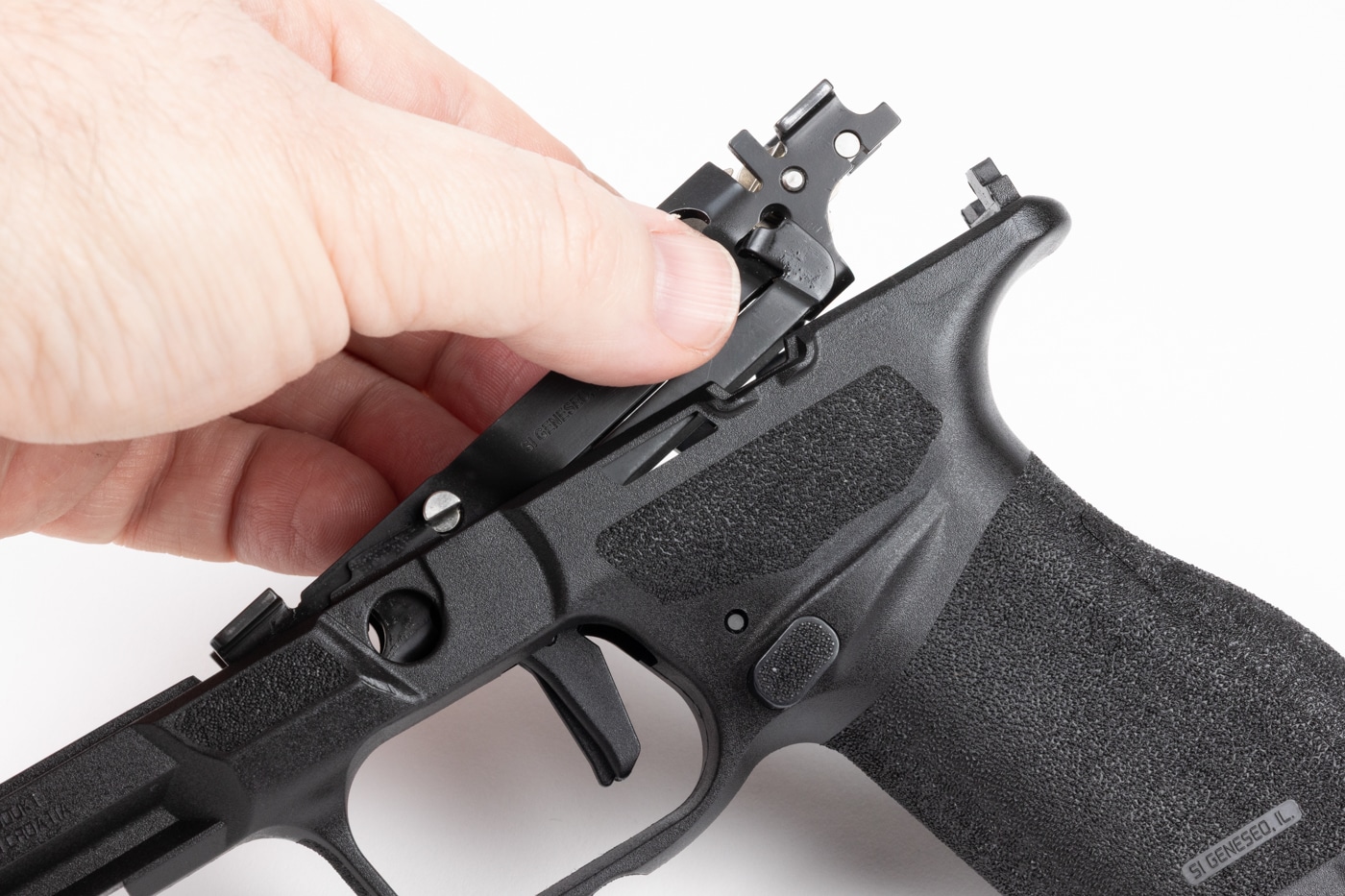 The image shows a hand lifting the rear portion of the Central Operating Group up and out of the Springfield Echelon 4.0C grip module. The front end of the assembly remains slightly hooked into the grip, while the rear is elevated, demonstrating the pivoting motion required for removal. The person’s other hand is gently pressing the trigger to help release the assembly, as recommended in Springfield’s instructions. The slide has been removed and the grip module is stabilized on a clean surface. This clear view shows how the Central Operating Group separates from the non-serialized polymer grip, emphasizing the modular design of the Echelon series. Good lighting highlights the mechanical parts and the careful technique used. This image is especially helpful for users learning to perform maintenance or swap grip modules on the Echelon 4.0C.