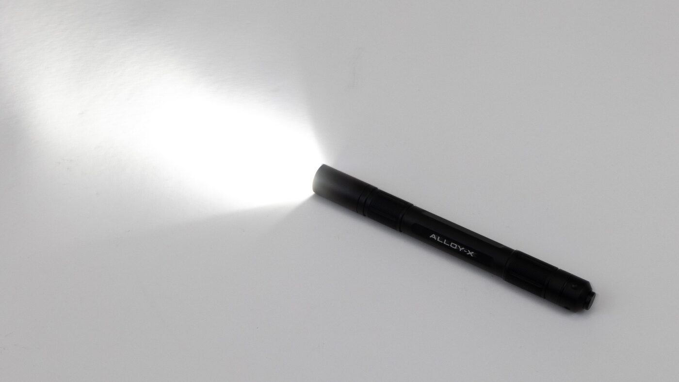 Image showing the Princeton Tec Alloy-X flashlight beam projected in a dark environment. The light throw is bright and evenly distributed, demonstrating its 400-lumen maximum output. The beam pattern leans toward a flood, covering a wide area instead of a narrow spot. Edges of the light fade smoothly without sharp cut-off lines. This type of beam is useful for everyday tasks such as searching, working, or navigating in low-light conditions. The photo highlights the effective illumination provided by the compact EDC flashlight.