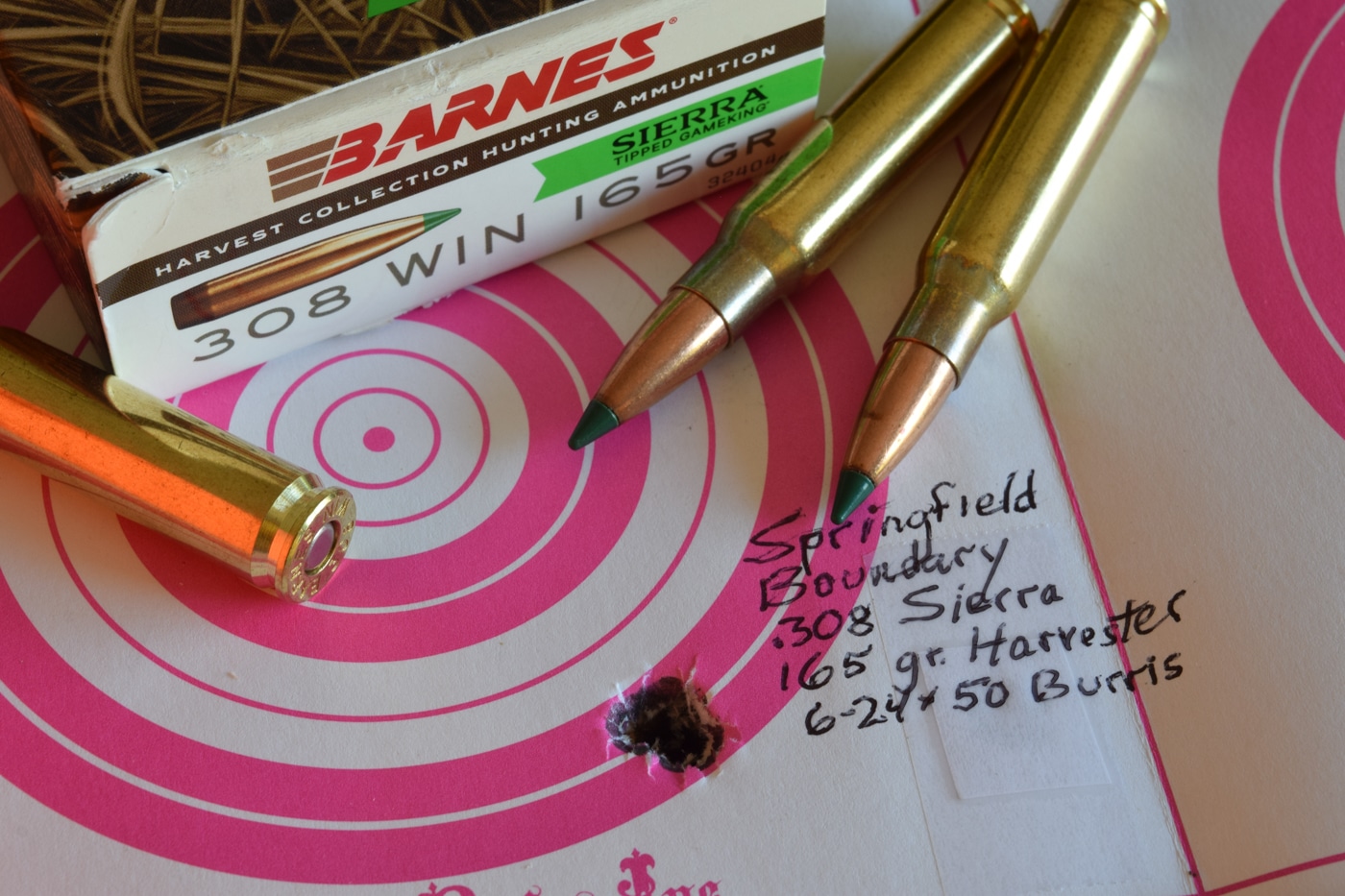 Paper target displaying an extremely tight three-shot group from a Springfield Armory Boundary rifle chambered in .308 Winchester. The holes overlap into a single ragged mark, indicating sub-MOA accuracy. This was achieved with Barnes Harvest Collection ammunition loaded with Sierra Tipped GameKing bullets. The target is attached to a backboard at an outdoor shooting range. Lighting and focus make the grouping clearly visible, underscoring the load’s consistency and precision.