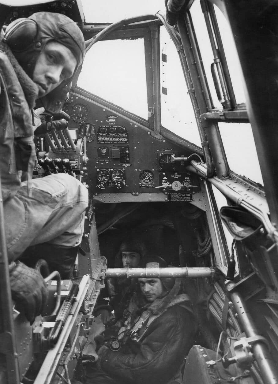 Interior view of a Handley Page Halifax during a World War II bombing mission, showing the pilot, navigator, and bombardier at their stations. The pilot is seated at the controls, focused on flying the large four-engine bomber. The navigator sits nearby with charts and plotting tools, guiding the crew toward their target. The bombardier, positioned at the front, prepares for the bomb run with his sighting equipment. The space is cramped, filled with instruments, wiring, and dim lighting suited for night operations. Each crew member’s task was essential, and their coordination determined the success and survival of the mission. The photograph highlights the human side of the Halifax’s operations, emphasizing the teamwork that made the bomber effective.