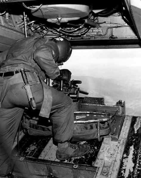 The image shows the rear gunner’s position on a Boeing ACH-47A “Guns-A-Go-Go” attack helicopter. The gunner is stationed at the lowered rear loading ramp, operating a mounted defensive machine gun. This position was typically armed with an M60D 7.62×51mm machine gun or a .50 caliber M2 Browning heavy machine gun, depending on mission requirements. The rear gunner’s role was to protect the aircraft from pursuing enemy forces during extraction or withdrawal. From this position, the gunner had a wide field of fire to the rear and slightly to the sides. The ACH-47A’s design allowed the rear ramp to serve both as a loading area and a defensive firing platform. The photograph highlights the gun mount, ammunition feed system, and the open view from the ramp.