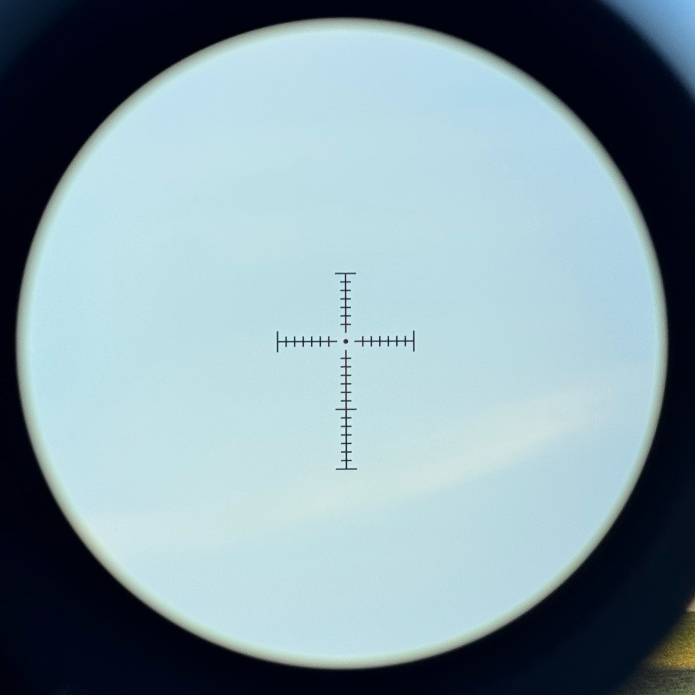 The image shows the view through an EOTECH Vudu 3-9X32 riflescope, with the HC1 MOA-based reticle centered on a target. The crosshairs are fine and clean, with hashmarks spaced for elevation and windage adjustments. Only the central portion of the reticle is illuminated, with a small red aiming dot in the middle for precise shots. The outer area of the reticle remains black for an uncluttered sight picture. The background target is slightly out of focus, emphasizing the reticle itself. This design supports both quick target acquisition and precision at medium ranges.