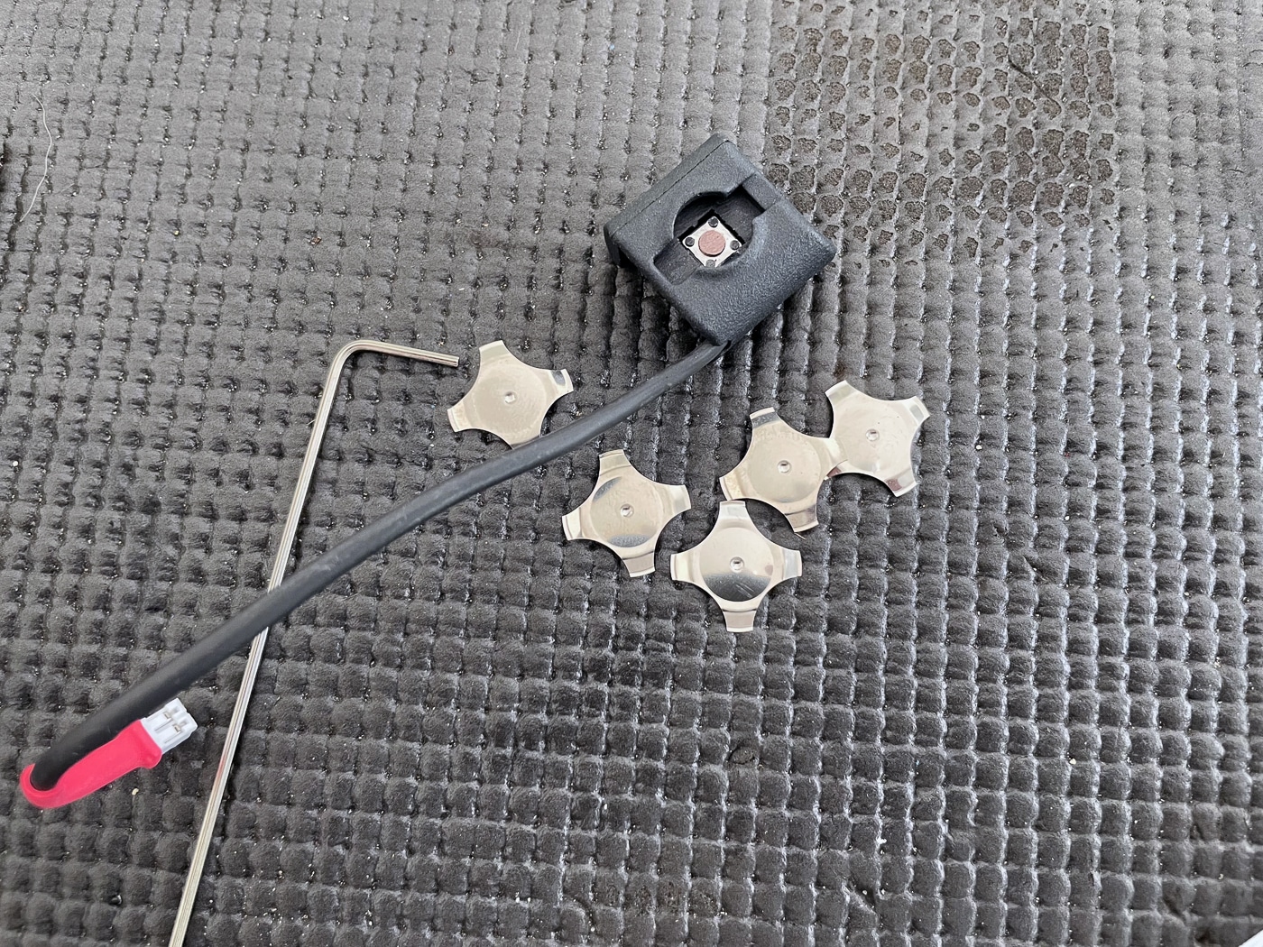 Several small, flat, star-shaped springs arranged on a clean surface. These springs are part of the Laser Ammo Flash Bolt dry-fire training system and are inserted into the trigger activation switch. Each spring adds to the trigger pull weight, allowing the user to match the feel of their real AR-15 trigger. When all five springs are installed, the maximum pull weight is about 5 pounds. The springs are made of thin metal and have a compact design for easy installation. This image highlights the simple yet effective way the Flash Bolt simulates realistic trigger resistance.