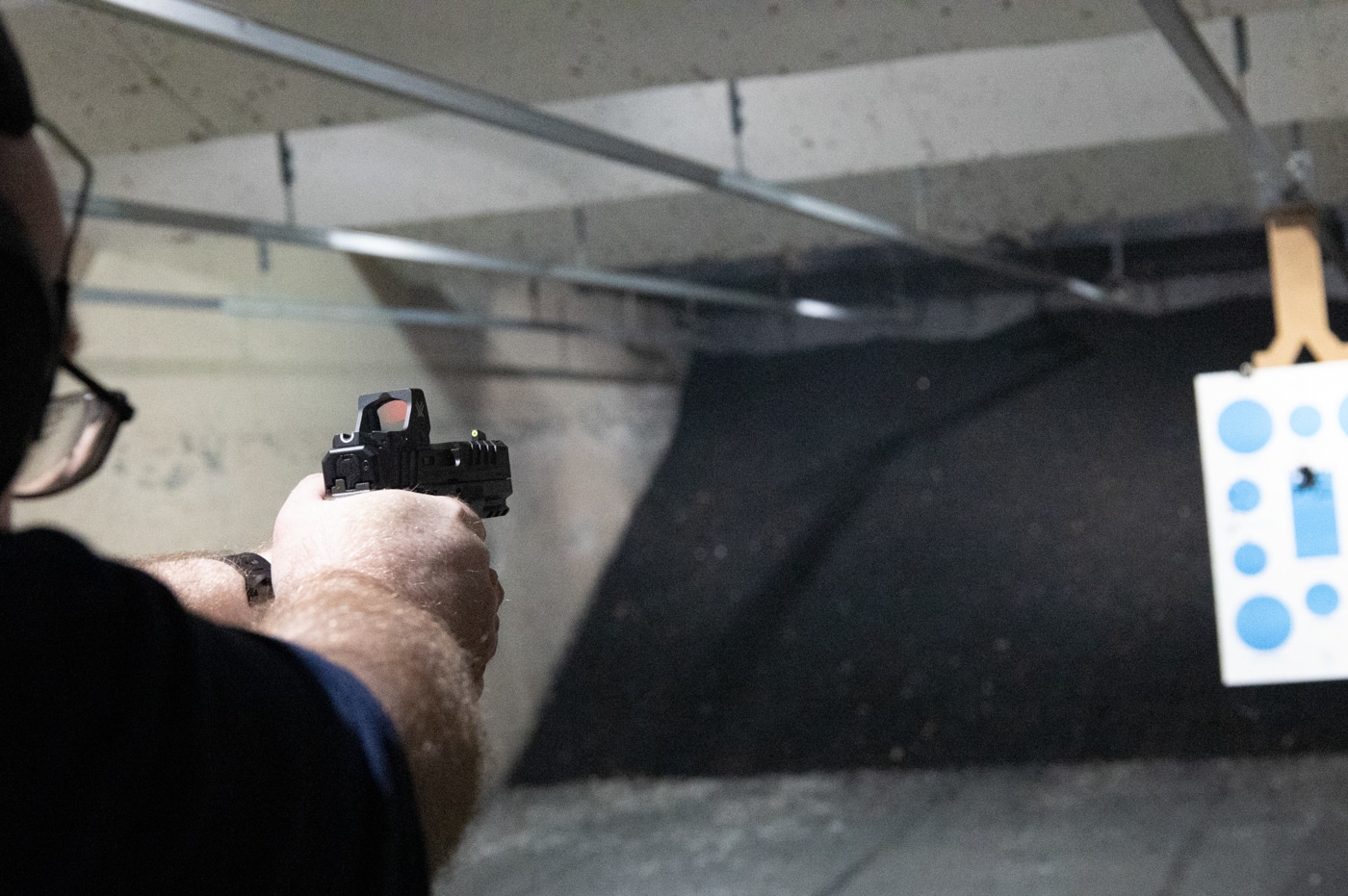 The image shows a shooter at an outdoor range test firing a Springfield Armory Echelon 4.0C with a recently swapped grip module. The hands are firmly gripping the pistol, and the shooter is in a proper stance with the firearm aimed downrange. The focus is on the grip area, highlighting the new grip module — its texture, color, and fit against the shooter’s hand are clearly visible. Expended shell casings may be seen in the air, indicating live fire. The background is a typical shooting range setting, with targets visible downrange and proper safety gear worn by the shooter. The image illustrates the importance of testing your firearm after making any changes, especially to the grip. It also demonstrates how grip swaps can impact handling and recoil management on the Echelon 4.0C.