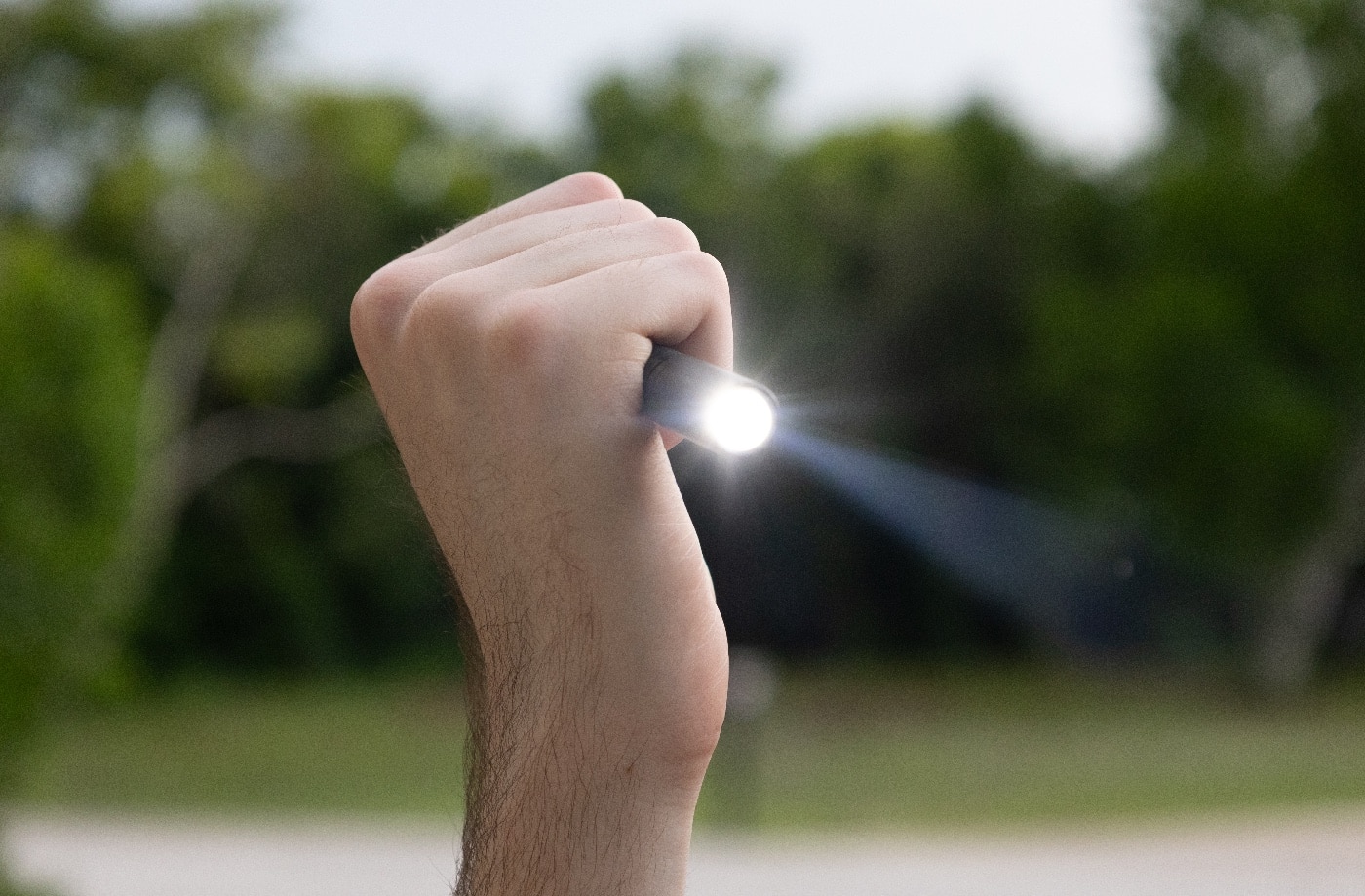 Photo of a person holding the Princeton Tec Alloy-X flashlight in their hand while using it. The slim pen light body fits naturally between the fingers, making it easy to carry and operate. The user’s thumb rests on the rear-mounted clicky button for simple activation. The light is illuminated, casting a bright beam forward to show its practical use in real-world conditions. The Alloy-X’s lightweight aluminum construction is evident, making extended use comfortable. This hand-held demonstration highlights the flashlight’s suitability as an everyday carry tool for both work and personal safety.