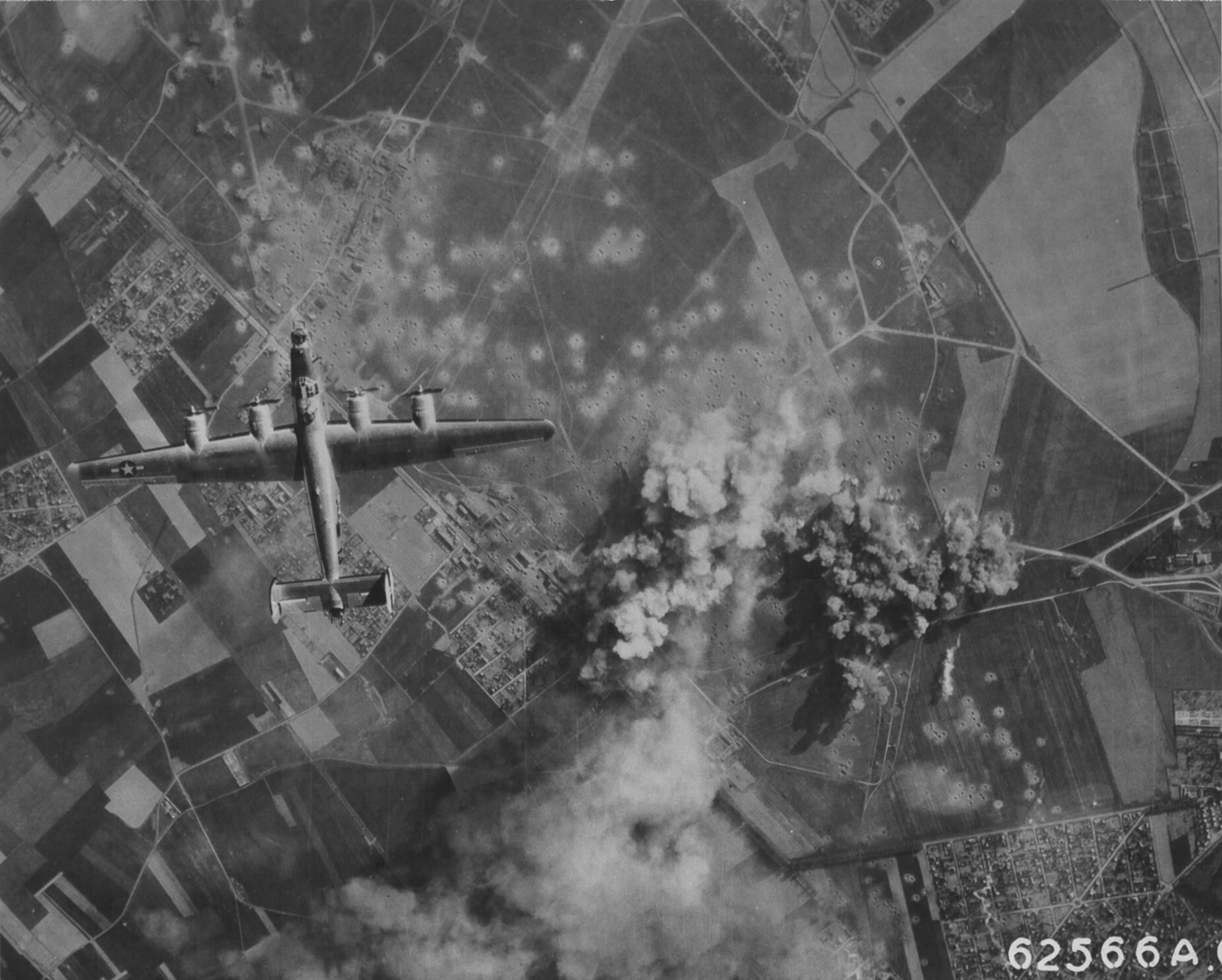 A U.S. Army Air Forces Consolidated B-24 Liberator bomber is shown releasing bombs over Orly Airport outside Paris in May 1944. Multiple bombs are captured mid-fall from the aircraft’s open bomb bay doors. Below, the airfield runways, hangars, and surrounding landscape are faintly visible as the target area. This mission was part of the pre-invasion bombing campaign that aimed to neutralize Luftwaffe airfields in occupied France. The B-24, with its heavy payload and long range, was ideally suited for these strikes. The image demonstrates how Allied bombers sought to weaken German defenses in advance of Operation Overlord. It provides a rare combat view of a Liberator in the act of bombing a strategic target.