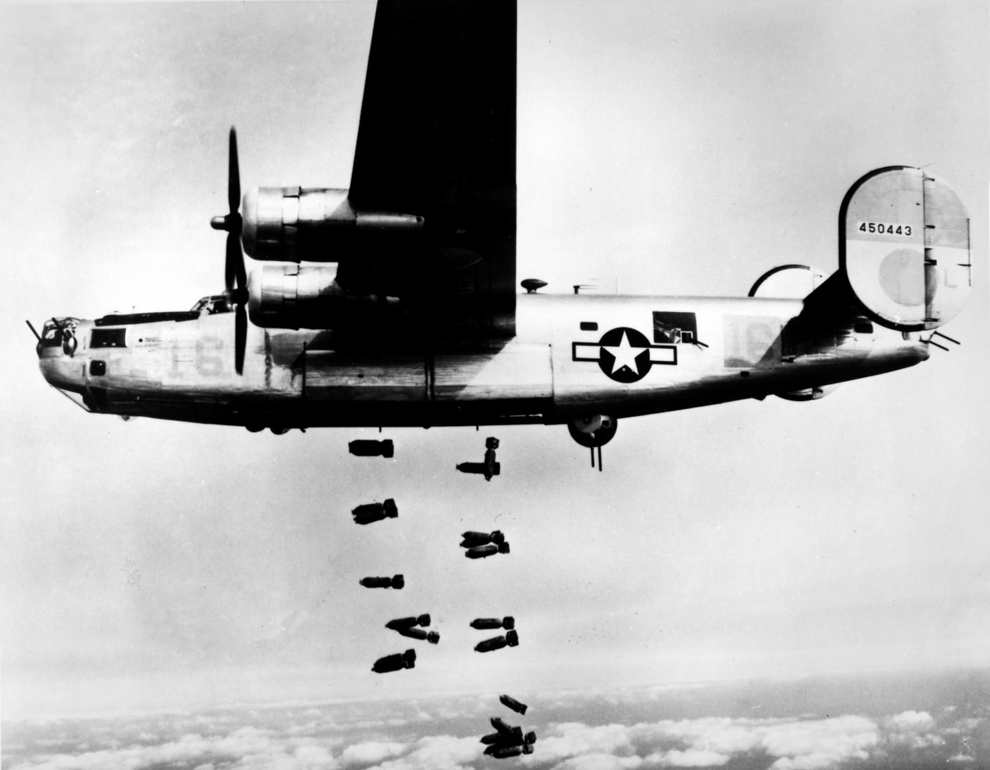 A dramatic wartime photograph shows a Consolidated B-24 Liberator of the U.S. 15th Air Force releasing bombs over the railyards at Muhldorf, Germany, on March 19, 1945. The aircraft flies at high altitude, and multiple bombs can be seen dropping toward the ground in a staggered formation. Below, the rail facilities and surrounding terrain are visible, marking the importance of the target to German logistics and supply. The photo captures the destructive power of heavy bombers in daylight precision raids late in the war. By this time, B-24s were essential to crippling transportation routes across the Third Reich. The image highlights the scale of Allied bombing efforts in the European theater. It underscores how airpower was used to weaken Germany’s war infrastructure in the final months of conflict.