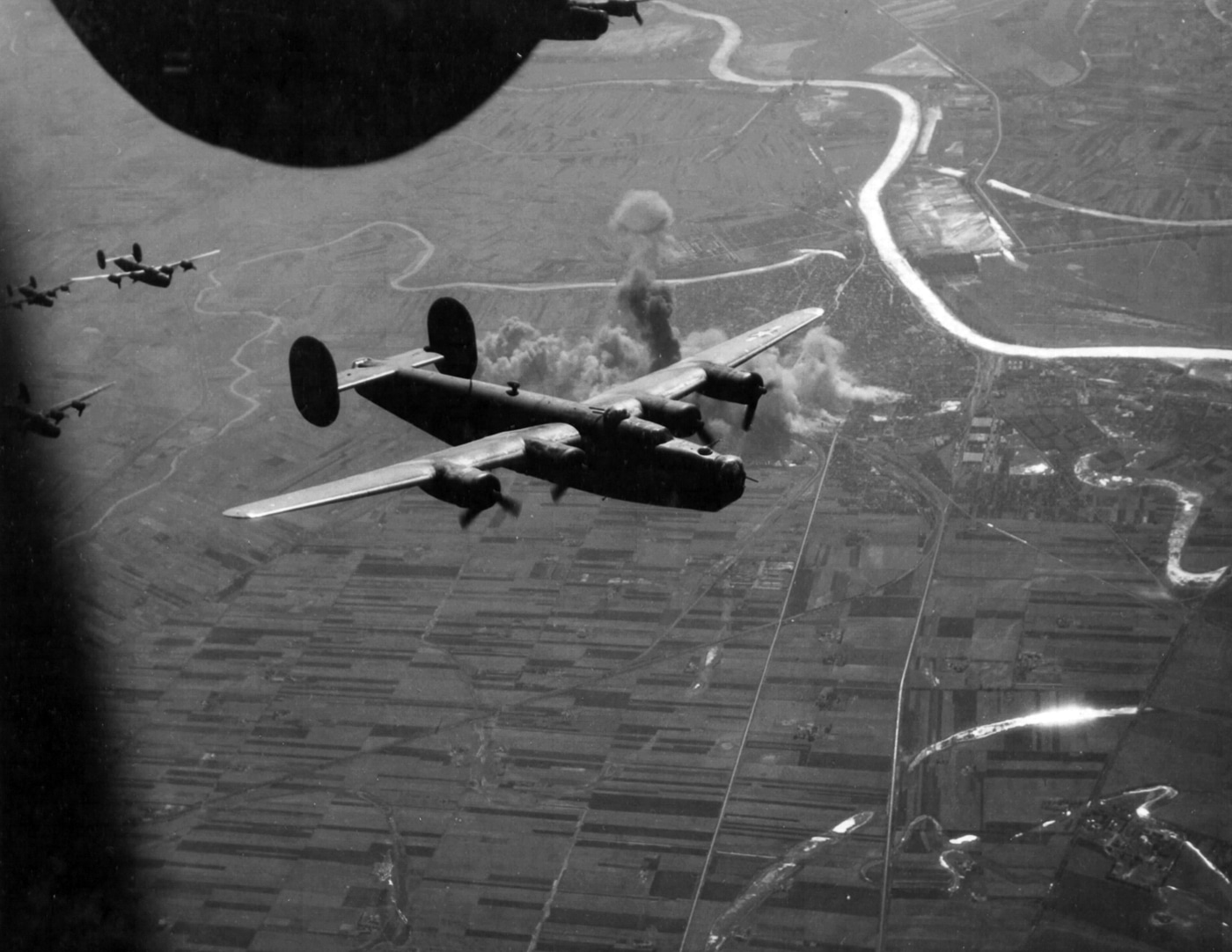A formation of Consolidated B-24 Liberators flies toward the Hungarian city of Szolnok in 1944 during World War II. The heavy bombers are shown at high altitude in tight formation, their contrails streaking across the sky. The mission targeted rail yards and industrial facilities, key nodes in the German supply network across Eastern Europe. Such raids were part of the broader Allied effort to weaken Axis transportation and logistics in preparation for advancing ground forces. The Liberators, with their long range and large payload, were suited to reach deep into enemy territory from bases in Italy. The photograph highlights both the size of the bomber streams and the coordinated nature of strategic air campaigns. It represents the increasing pressure on Axis infrastructure in the later years of the war.