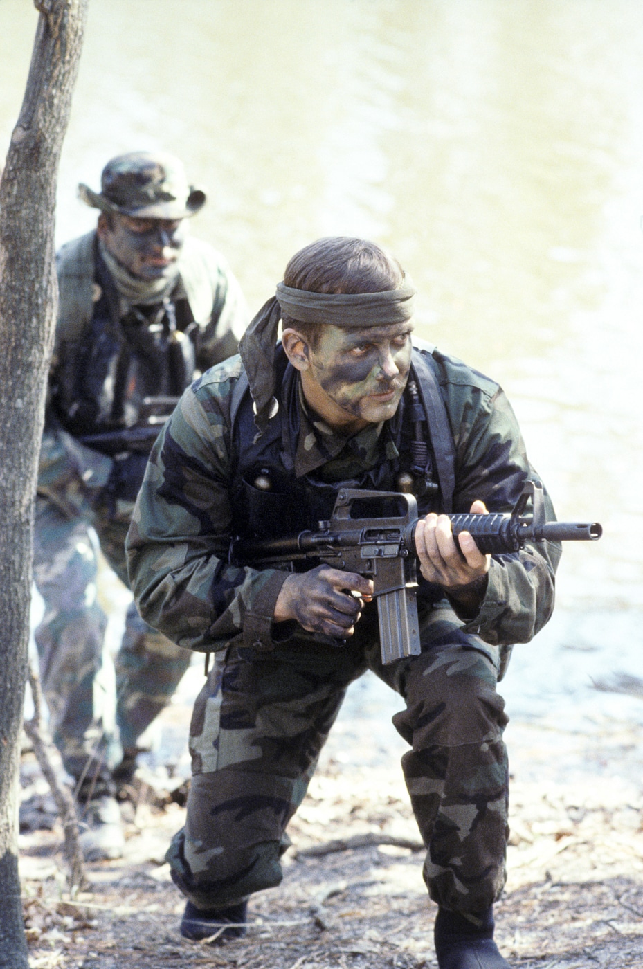 Image of U.S. Navy SEALs in 1985 training with CAR-15 rifles, also identified as XM177 carbines. The rifles are shown with collapsible aluminum stocks extended, short barrels fitted with moderator muzzle devices, and standard 20- and 30-round 5.56mm magazines. Several weapons are lined up alongside training gear such as helmets, load-bearing vests, and web belts. Lighting and shadows suggest an outdoor or shipboard training space, typical for SEAL field drills during the 1980s. The XM177 carbines appear compact compared to the full-length M16A1 rifles, illustrating their advantage in close-quarters combat. This description includes keywords such as XM177, CAR-15, SEAL training, compact 5.56 carbine, collapsible stock, and Vietnam-era rifle variant for accessibility and SEO optimization.