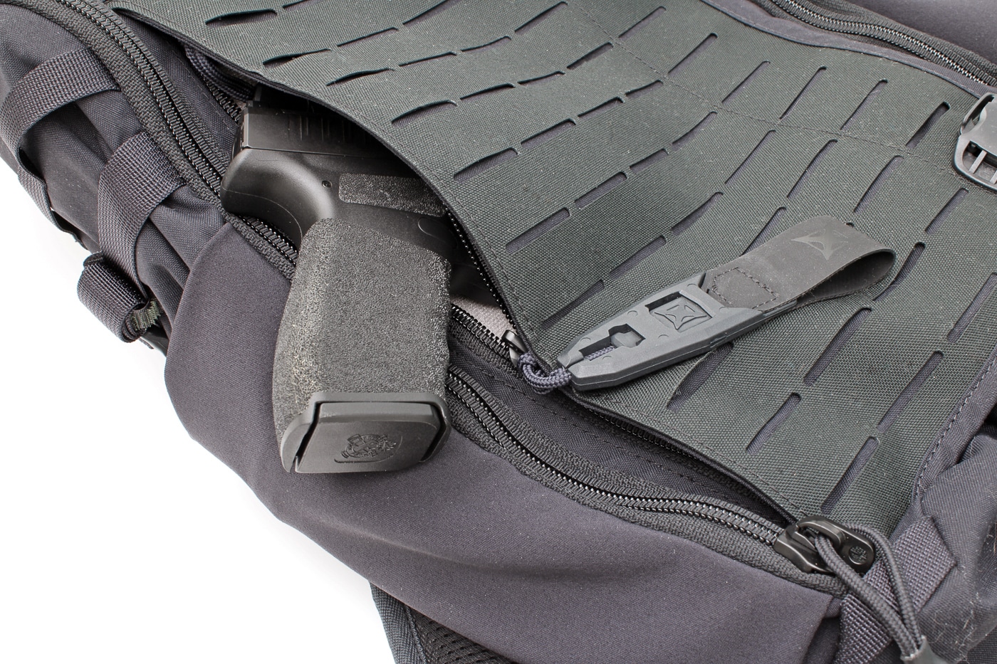 Close-up image of the Vertx Siege 25L EDC pouch opened via a rapid-access pull, revealing a Springfield Hellcat Pro 9mm pistol seated inside the loop-lined pocket. The black pouch interior and Velcro-lined surfaces show how the handgun and a hook-backed holster can be secured for retention. Visible zipper pulls and overlapping rings indicate the pouch can be locked for transport. Padded fabric and reinforced stitching around the pouch suggest durability for everyday carry and travel. The photo demonstrates how the pack supports concealed carry while allowing fast access when needed. Keywords: EDC pouch, rapid access, Hellcat Pro, concealed carry, loop-lined pocket.
