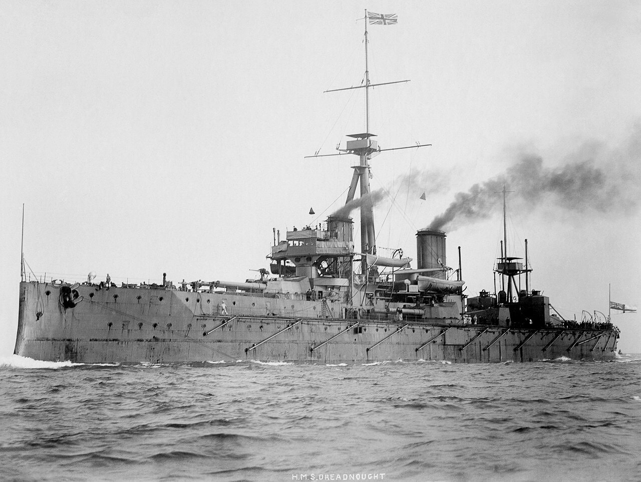 The photo shows HMS Dreadnought, the Royal Navy warship launched in 1906, sailing at sea. The ship has a long steel hull, multiple heavy gun turrets, and a distinctive superstructure that made her the most advanced battleship of her time. She was the first “all big gun” warship and the first capital ship powered entirely by steam turbines, which gave her superior speed and firepower. HMS Dreadnought rendered all previous battleships obsolete almost overnight, leading to a naval arms race before World War I. The photo captures her early years when she represented unmatched naval supremacy. Despite her revolutionary design, she never fired her guns in a major surface battle and was scrapped after just over a decade of service. This image highlights both her historic importance and the irony of her short-lived dominance.
