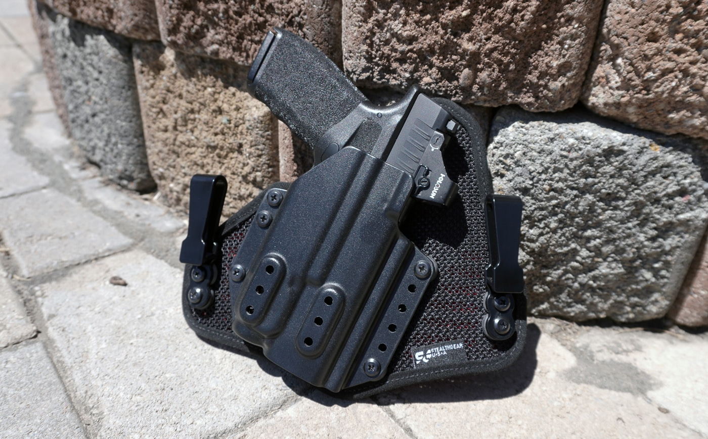 Close-up photo of a Springfield Hellcat Pro pistol secured inside a StealthGearUSA Ventcore 2.0 IWB Mini holster. The handgun is equipped with a red dot sight and a mounted Streamlight TLR-7A light, showing the holster’s compatibility with optic- and light-bearing setups. The Kydex shell is molded tightly around the pistol frame for retention, with smooth, rounded edges visible. The padded Ventcore backing rests against the body side, designed for comfort and breathability. The image emphasizes how the holster accommodates modern concealed carry firearms. Lighting and detail highlight both the gun and holster clearly.