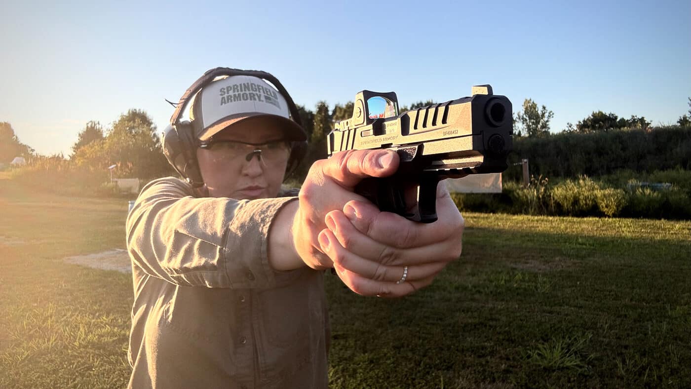 A competitive shooter is testing the Trijicon RMR reflex sight with a green LED dot reticle during live fire. The optic’s patented protective ears and compact design are visible on the handgun slide. The green reticle offers improved visibility compared to red, especially in bright light and challenging visual backgrounds. This optic is trusted by military, law enforcement, hunters, and competition shooters for its reliability and long battery life. The shooter is evaluating how the reticle performs against various targets. The scene emphasizes accuracy, speed, and confidence when using the RMR Green in action.