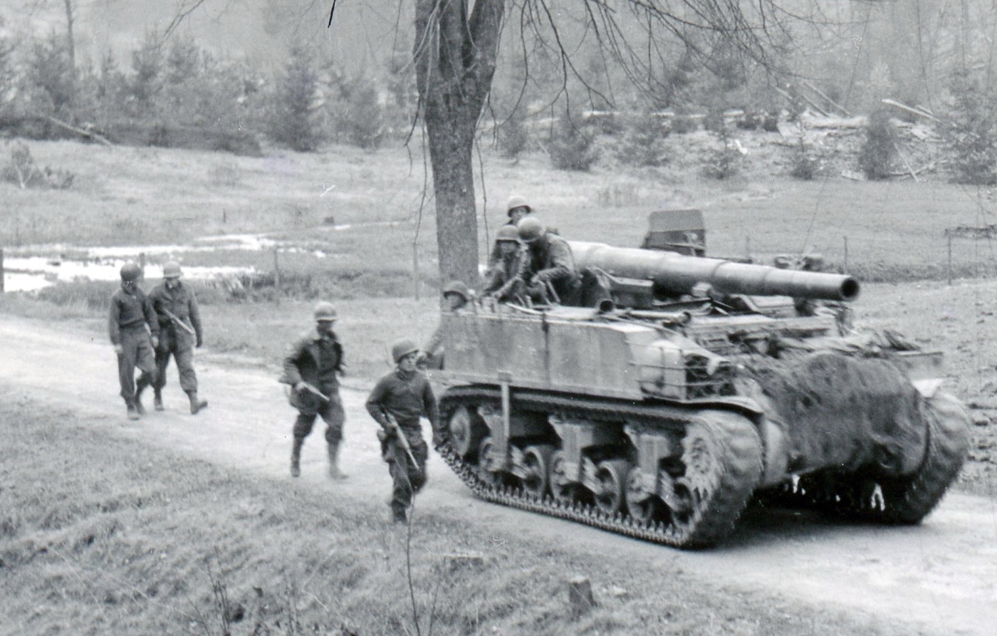 An M12 Gun Motor Carriage is pictured advancing through Germany in the spring of 1945, carrying its 155mm gun into position. The vehicle is based on the M3 tank chassis, stripped of a turret and fitted with a massive artillery piece. The crew compartments are open-topped, leaving the soldiers almost completely exposed to enemy fire. Unlike tanks, the M12 offered no real armor for protection, forcing the men to rely on positioning and supporting units for safety. Despite this, the gun’s destructive power against bunkers and fortified positions made it invaluable. The limited armor protection highlights the design compromise between mobility and firepower. This photograph reflects the vulnerability of artillery crews even while operating one of the most powerful American self-propelled guns of World War II.