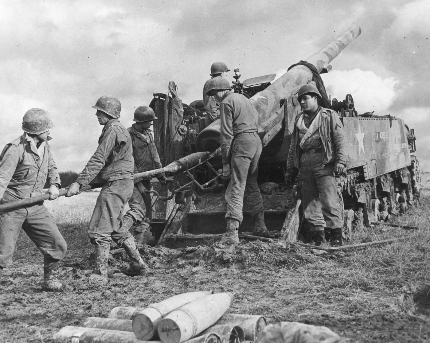 An American M12 Gun Motor Carriage is pictured in Germany during 1945, serving its 155mm M1918 gun in combat. The crew is operating the weapon, which fired massive 95-pound projectiles at a high muzzle velocity of 2,411 feet per second. The open rear crew compartment leaves the men exposed, but the vehicle’s power made it effective against German bunkers and fortifications. The M12 could manage only about two rounds per minute, reflecting the difficulty of loading such heavy ammunition. With only ten shells stored on board, resupply was critical to sustained operations. The M30 cargo carrier was usually paired with the M12 to bring additional rounds and propellant charges to the front. This scene captures the logistical and tactical challenges of using one of America’s most powerful artillery vehicles in the closing months of the war.