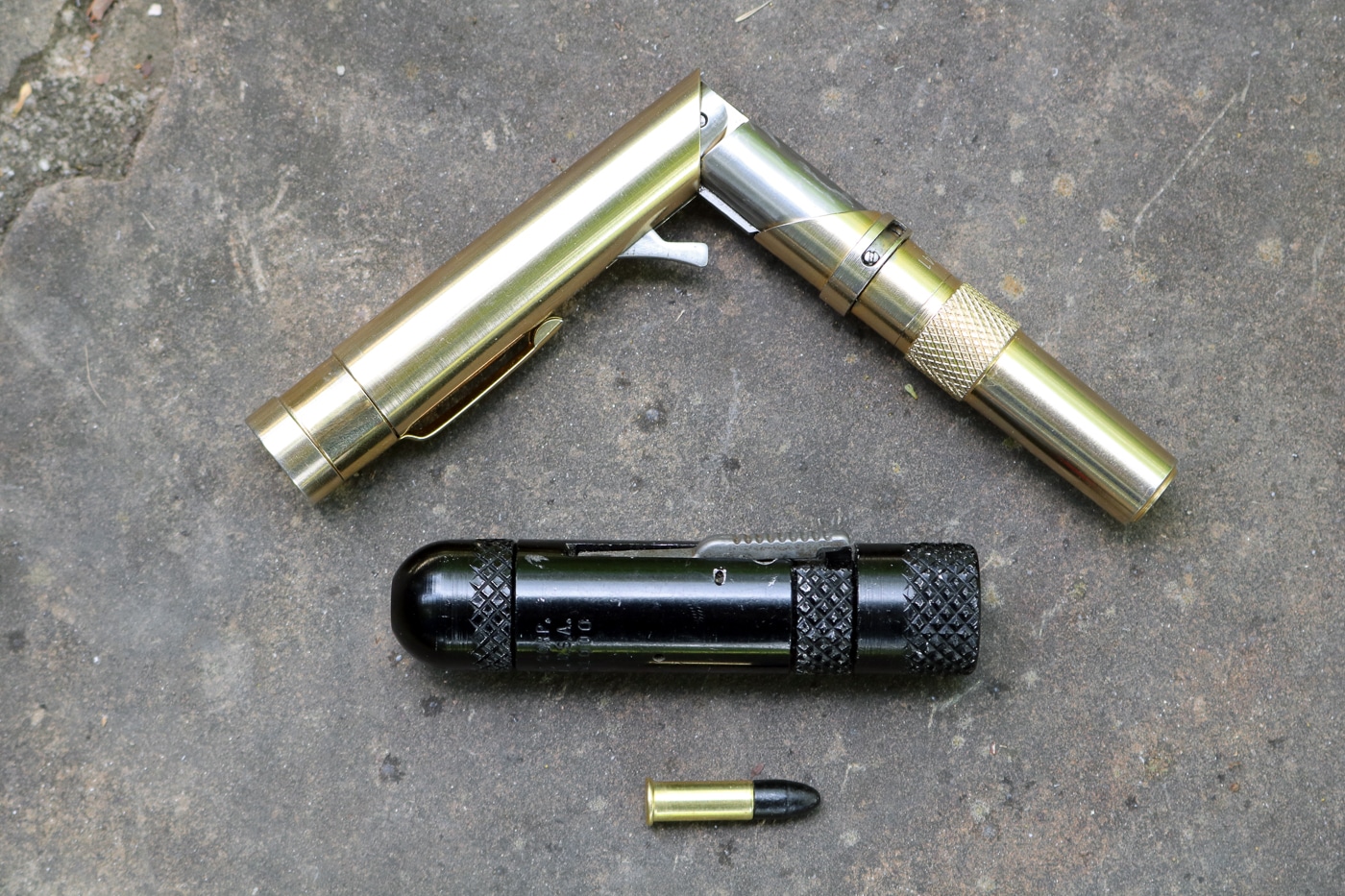 The image shows two small firearms side by side: the MAC Stinger on the bottom and the Braverman Stinger pen gun above it. The MAC Stinger has a short tubular shape, measuring just over three inches long, while the Braverman pen gun resembles an actual writing instrument when folded. Both are highly concealable weapons designed to fire .22 caliber rounds. The MAC Stinger was manufactured by the Military Armament Corporation in the 1970s, while the Braverman design came later and maintained a more pen-like profile. These compact guns were intended for covert use but were often considered impractical and unsafe. Their unusual designs place them in the BATF’s “Any Other Weapon” category. The photo emphasizes their small size and unusual appearance compared to traditional pistols.