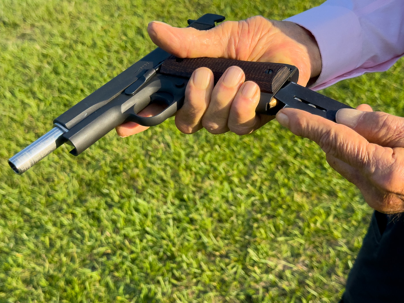The photo shows Massad Ayoob holding a Springfield Armory 1911 pistol while demonstrating the correct way to insert a magazine. His hands are positioned to guide the magazine into the well at the proper angle, a detail that reduces the risk of feeding issues. The firearm is angled slightly to allow viewers to see the mag well opening clearly. Ayoob’s attention is on hand placement and smooth technique. The demonstration emphasizes reliability during reloads, a critical skill in both defensive and competitive shooting. The image captures the moment before the magazine locks into place, showing step-by-step instruction. This helps illustrate the importance of consistent magazine insertion for the 1911 platform.