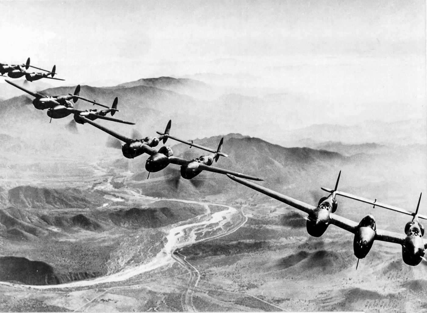 Black-and-white photograph of several Lockheed P-38 Lightning fighter planes flying in tight formation over the Southwest Pacific in April 1943. The aircraft are seen from above, their twin-boom design clearly visible against the backdrop of clouds and ocean. These long-range fighters had been recently introduced to the Pacific theater and were already proving decisive in air superiority battles. The formation flight demonstrates how U.S. Army Air Forces organized coordinated missions, often sending entire squadrons on interception or escort duty. By spring of 1943, the P-38 was one of the only Allied fighters capable of reaching deep into Japanese-controlled areas. The aircraft in this photo likely belonged to units later involved in Operation Vengeance.