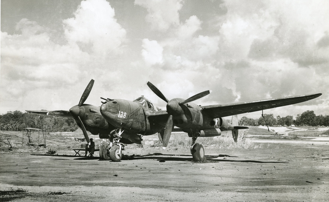 Black-and-white photograph of a Lockheed P-38 Lightning parked on an airstrip at Guadalcanal during World War II. The fighter’s distinctive twin-boom design is visible against the rough, improvised runway surface common to Pacific bases. Ground crew and equipment can be seen nearby, reflecting the constant maintenance needed in tropical conditions. Guadalcanal served as a forward operating base for the U.S. Army Air Forces, allowing P-38s to fly long-range interception and escort missions. It was from this island that the fighters launched the April 1943 Operation Vengeance mission against Admiral Yamamoto. The image highlights both the rugged conditions and the strategic role of Guadalcanal in the Pacific campaign.