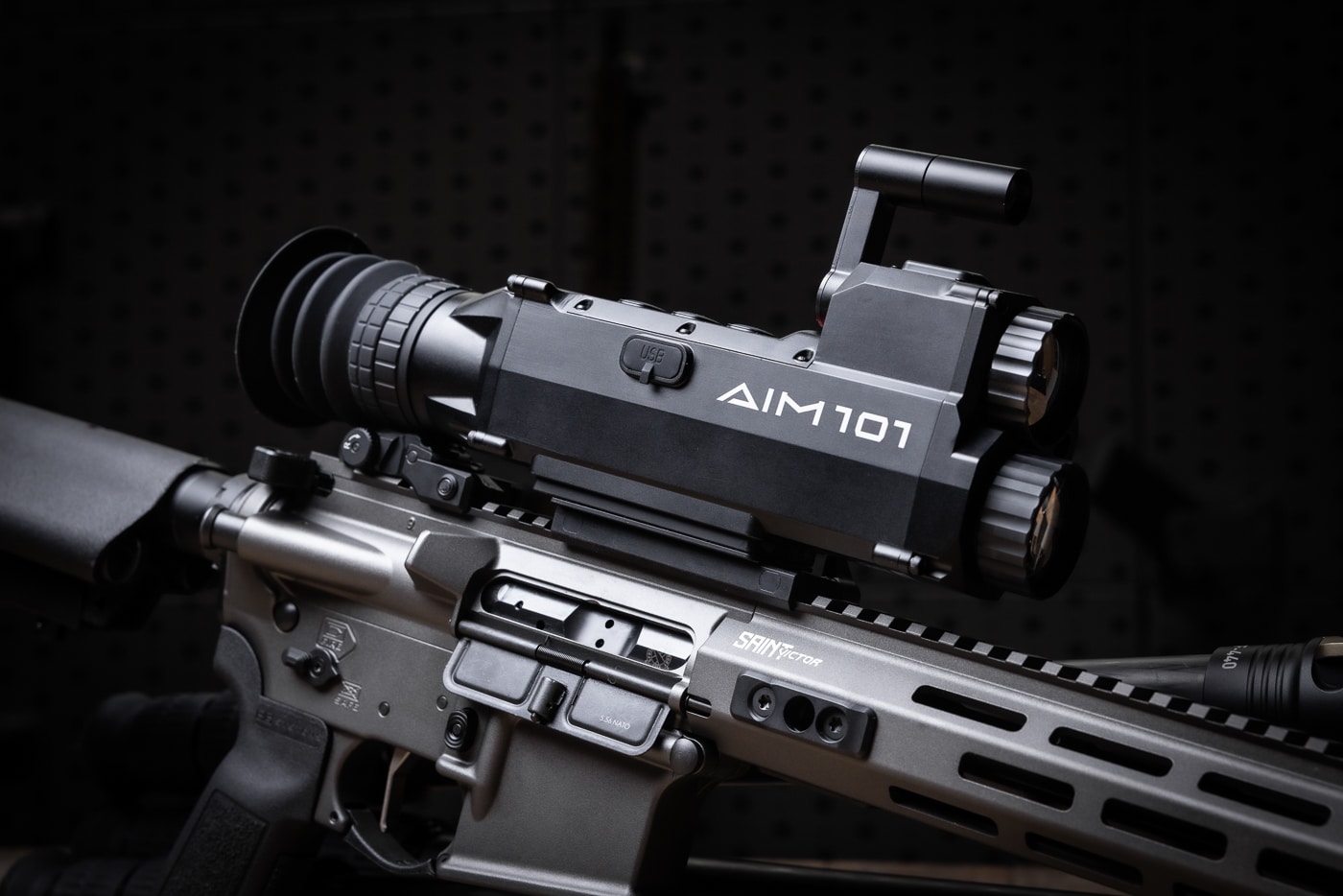 The photo shows a Springfield Armory SAINT rifle equipped with the Shinenyx AIM-101 fusion optic. The scope is securely mounted on the top rail and ready for live-fire use. The AIM-101’s housing, scroll wheel, and button layout are visible, showing its straightforward design. Its eyepiece extends back toward the shooter for comfortable use and a wide LCD view. The rifle rests in a controlled range environment, emphasizing durability and recoil management. This combination highlights how the AIM-101 works as a weapon-mounted thermal and digital night vision scope. The setup demonstrates the optic’s ability to deliver detection, identification, and hybrid fusion modes in a real-world shooting scenario.