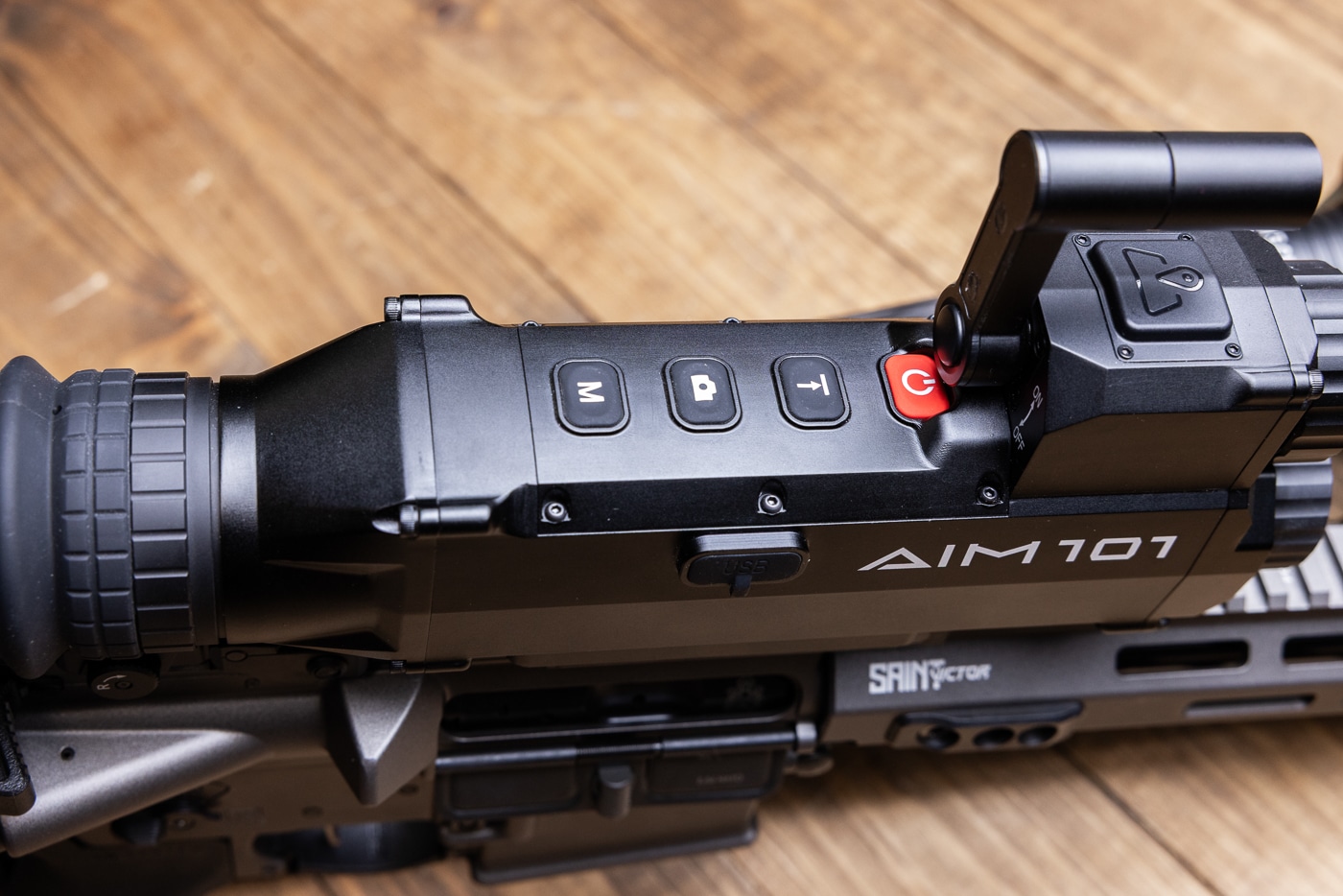 The image shows the top controls of the Shinenyx AIM-101 thermal and night vision fusion optic. Four large rubberized buttons are arranged across the housing, each with clear markings for power, laser range finding, video capture, and mode switching. The buttons are slightly raised, making them easy to feel and press even when wearing gloves. Their placement along the top makes quick adjustments simple in low-light environments. The surrounding housing is all-metal with a rugged matte finish, built to handle recoil and field use. This view emphasizes the AIM-101’s user-friendly interface and durability. The layout eliminates the need for deep menu navigation when fast changes are required in dynamic situations.
