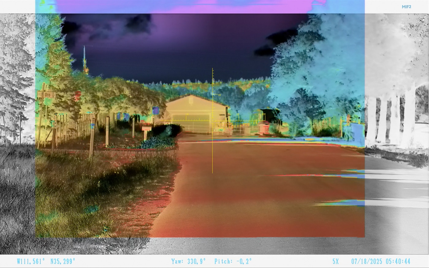 The image is a captured FusionView display from the Shinenyx AIM-101, showing land with a building in the scene. The building is clearly visible through digital night vision detail, while thermal overlays highlight heat sources in the area. The ground and surrounding terrain are rendered in low-light tones, providing environmental context. This hybrid view allows the operator to identify both man-made structures and potential heat signatures at the same time. Fusion mode emphasizes the contrast between warm and cool elements without losing background clarity. This type of imaging is useful for surveillance, property security, and scanning open land. The display shows how the AIM-101 balances detection with situational awareness.