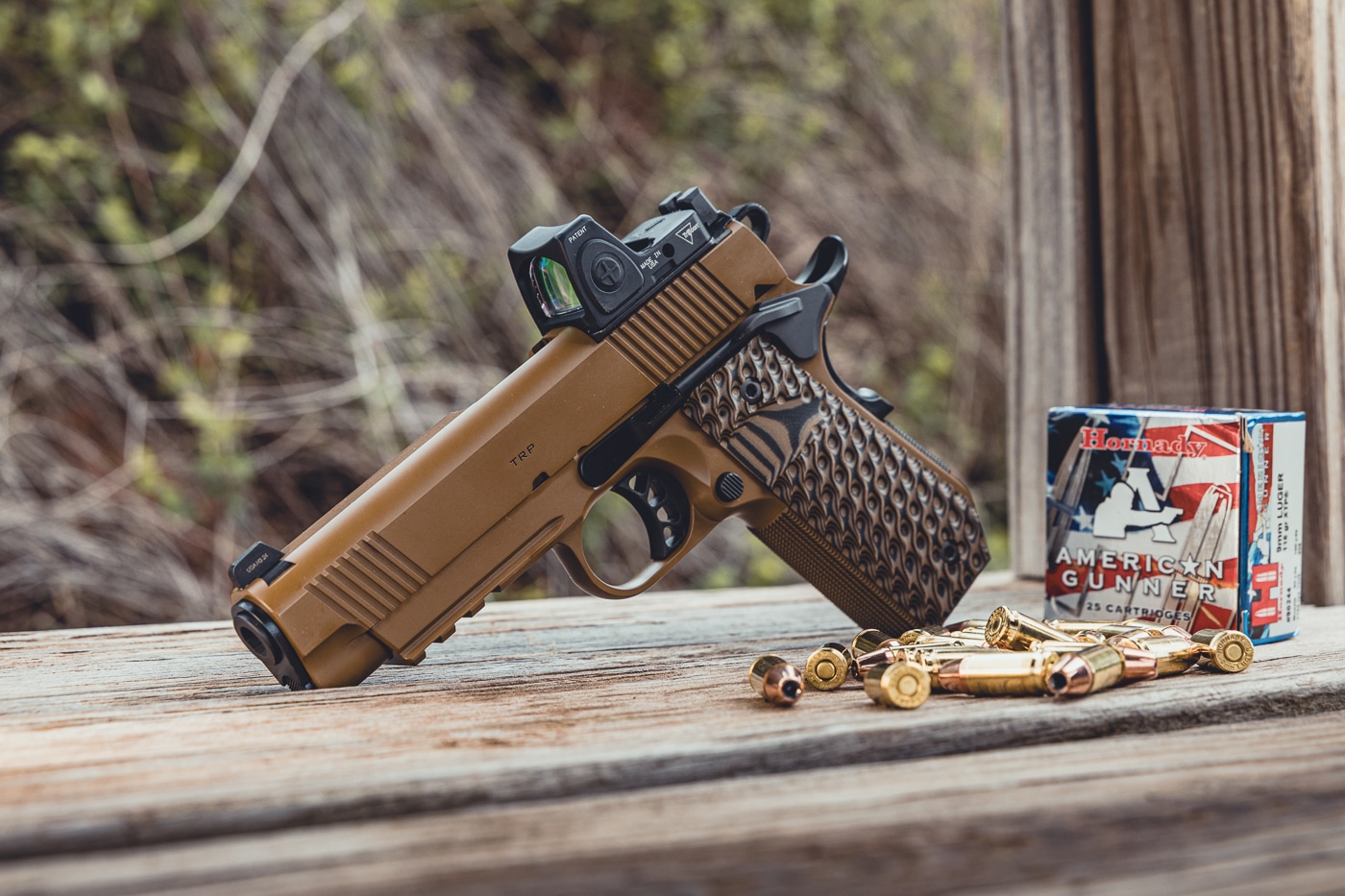 This photo features a Springfield Armory 1911 TRP AOS pistol equipped with a Trijicon RMR red dot sight. The handgun is displayed alongside Hornady American Handgunner ammunition, emphasizing its role as a precision firearm for defensive or range use. The pistol has a forged slide and frame, forward serrations, skeletonized trigger, and G10 grips, reflecting the TRP series’ upgraded features. The RMR optic highlights the adaptability of the Agency Optic System, which allows shooters to mount optics without custom work. The Hornady ammo reinforces the combination of modern firearm technology and high-quality defensive ammunition. This image conveys readiness, performance, and innovation within the 1911 platform.