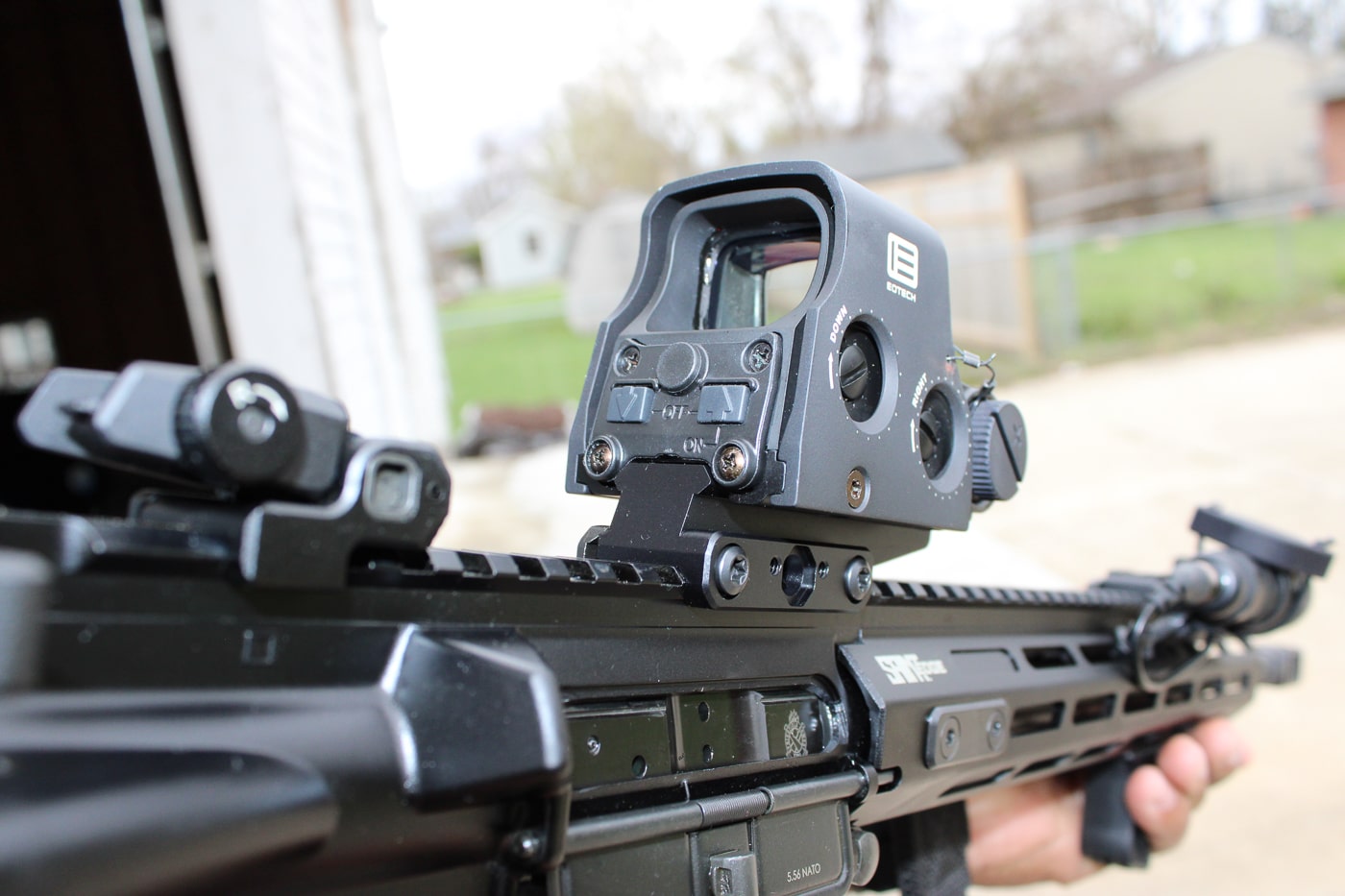 Photograph of a Springfield Armory SAINT rifle laid horizontally on a neutral surface, shown as a bug-out gun option for emergency preparedness. The AR-style lower and upper receiver are visible along with the collapsible stock and a standard 5.56 magazine seated in the magwell. The M-LOK free-floating handguard and rail system are clear, suggesting accessory mounting points for lights or optics. This image is useful for articles about Springfield Armory bug out guns, home defense rifles, and compact long-gun choices. Textures on the grip and receiver are visible, conveying a durable, serviceable finish rather than a decorative look. No people are present and the background is intentionally plain to keep focus on the SAINT’s features.