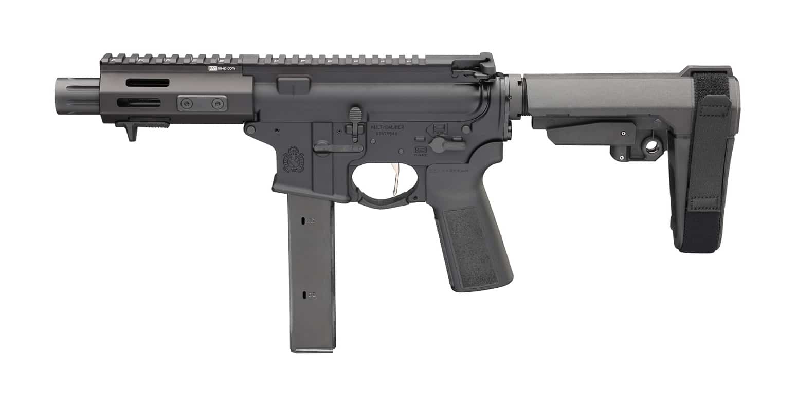 Image shows a Springfield Armory SAINT 9mm pistol laid out on a neutral surface to display its compact carbine layout and controls. The photograph clearly reveals the short 5.5-inch barrel, slim handguard, and a low-profile red dot optic mounted on the top rail. The collapsed pistol brace is visible at the rear, illustrating reduced overall length for easier movement in confined spaces such as hallways and vehicles. This composition highlights the SAINT Victor 5.5” 9mm as a practical option for home defense, urban survival, and CQB scenarios where a full-length rifle would be unwieldy. Viewers can note the ergonomic pistol grip and accessible magazine well designed for quick reloads under stress.