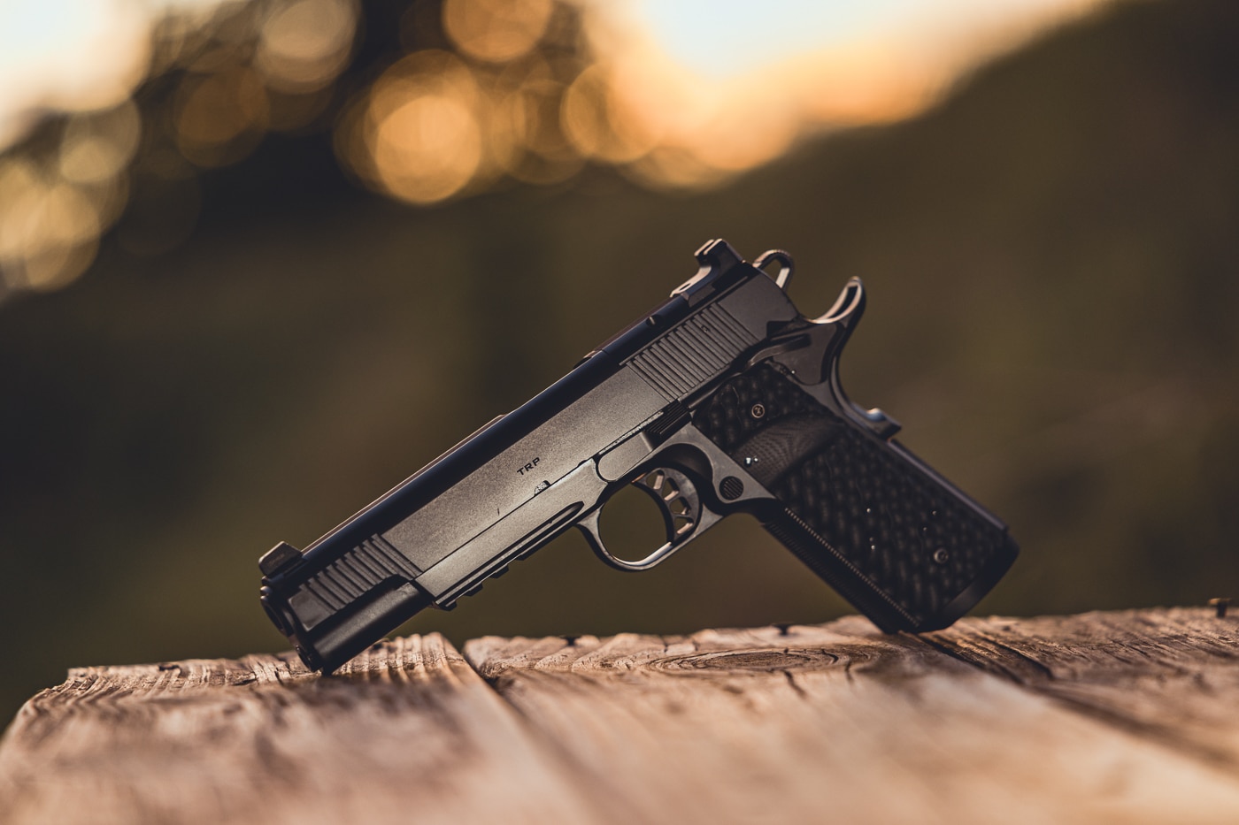 This photo shows a Springfield Armory 1911 TRP AOS pistol resting on a shooting bench in its iron sight configuration. The handgun is equipped with its cover plate installed over the optic cut, keeping the traditional rear sight in place. The pistol’s matte finish, front strap checkering, and textured G10 grips are clearly visible. Positioned in a range setting, the pistol is laid out for inspection or ready use. The photo emphasizes the reliability and simplicity of shooting with iron sights, while showing how the TRP AOS maintains a clean slide profile without an optic. This image conveys the traditional shooting experience paired with Springfield’s premium build quality.