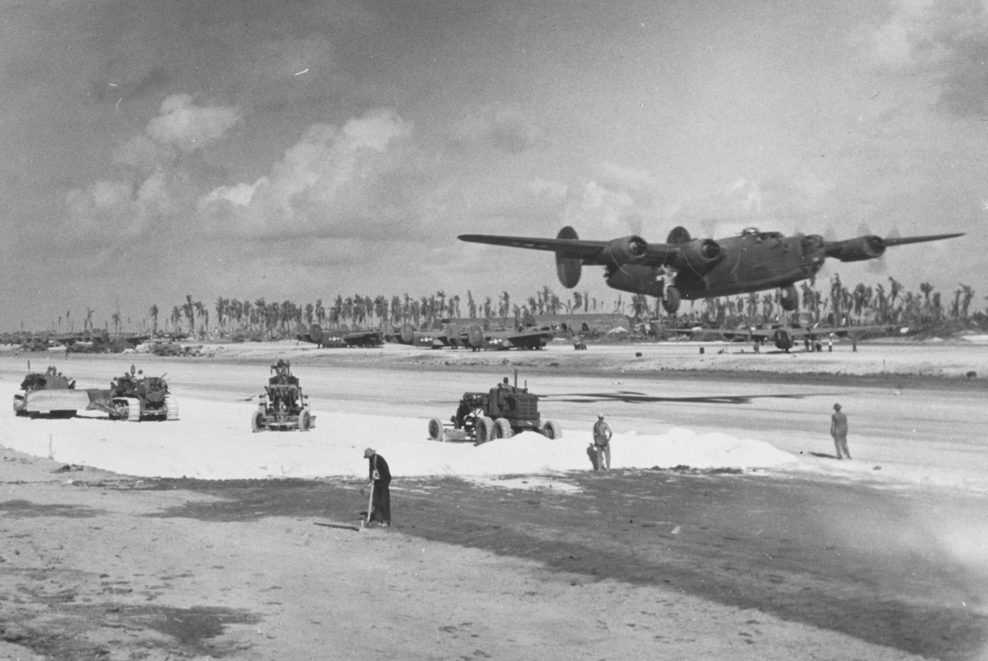 A U.S. Army Air Forces Consolidated B-24 Liberator bomber is captured mid-takeoff from an airfield on Eniwetok Island, Marshall Islands, on April 13, 1944. In the foreground, U.S. Navy Seabees are seen spreading crushed coral to widen and reinforce the runway surface. The freshly cleared island base shows other parked B-24 bombers in the distance, waiting for their own missions. The Seabees’ efforts highlight the critical engineering work that allowed heavy bombers to operate from remote Pacific atolls. This construction enabled long-range strikes deep into Japanese-held territory. The image combines both combat aviation and the behind-the-scenes labor that sustained it. It demonstrates how logistics and engineering supported the air war in the Pacific Theater.