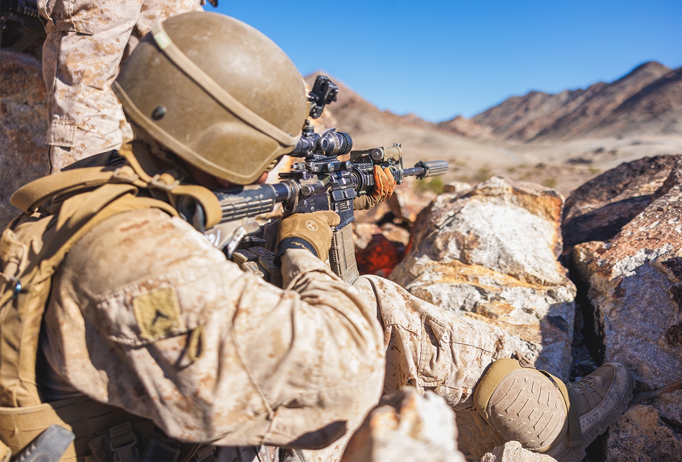 The photograph shows a US Marine armed with an M4 carbine during training operations at Twentynine Palms, California, illustrating what is a carbine that serves as the primary weapon for modern American military personnel. The M4 carbine represents perhaps the most recognizable and widely adopted carbine in contemporary military service worldwide. This firearm features a 14.5-inch barrel, significantly shorter than the 20-inch barrel of the M16A2 rifle it largely replaced in frontline service. The Marine's M4 demonstrates the carbine's compact overall dimensions that enable rapid maneuvering through buildings, vehicles, and varied terrain encountered in modern combat operations. The M4 fires 5.56×45mm NATO ammunition, maintaining substantial stopping power and effective range while offering improved handling characteristics over full-size rifles. The carbine visible in the image incorporates modern features including a telescoping stock for adjustable length of pull, a flat-top receiver for mounting optical sights, and accessory rails for attaching lights, lasers, and foregrips. Twentynine Palms serves as a major training facility where Marines practice combat skills with their issued weapons in realistic desert environments. This photograph captures the M4 carbine in its intended military application, demonstrating why this weapon platform has become standard equipment for American soldiers and numerous allied forces worldwide.